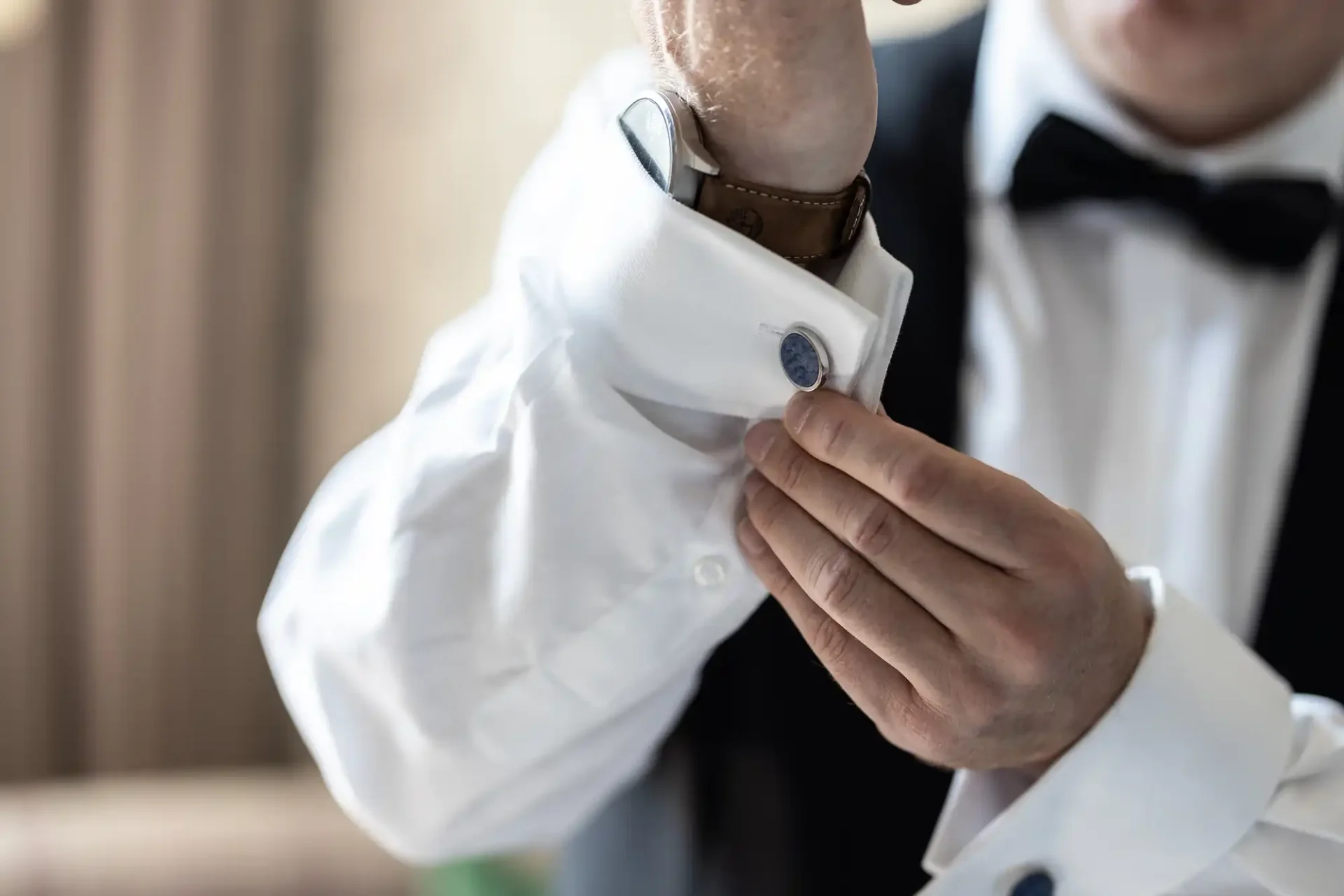 A man in a tuxedo adjusts his cufflink.