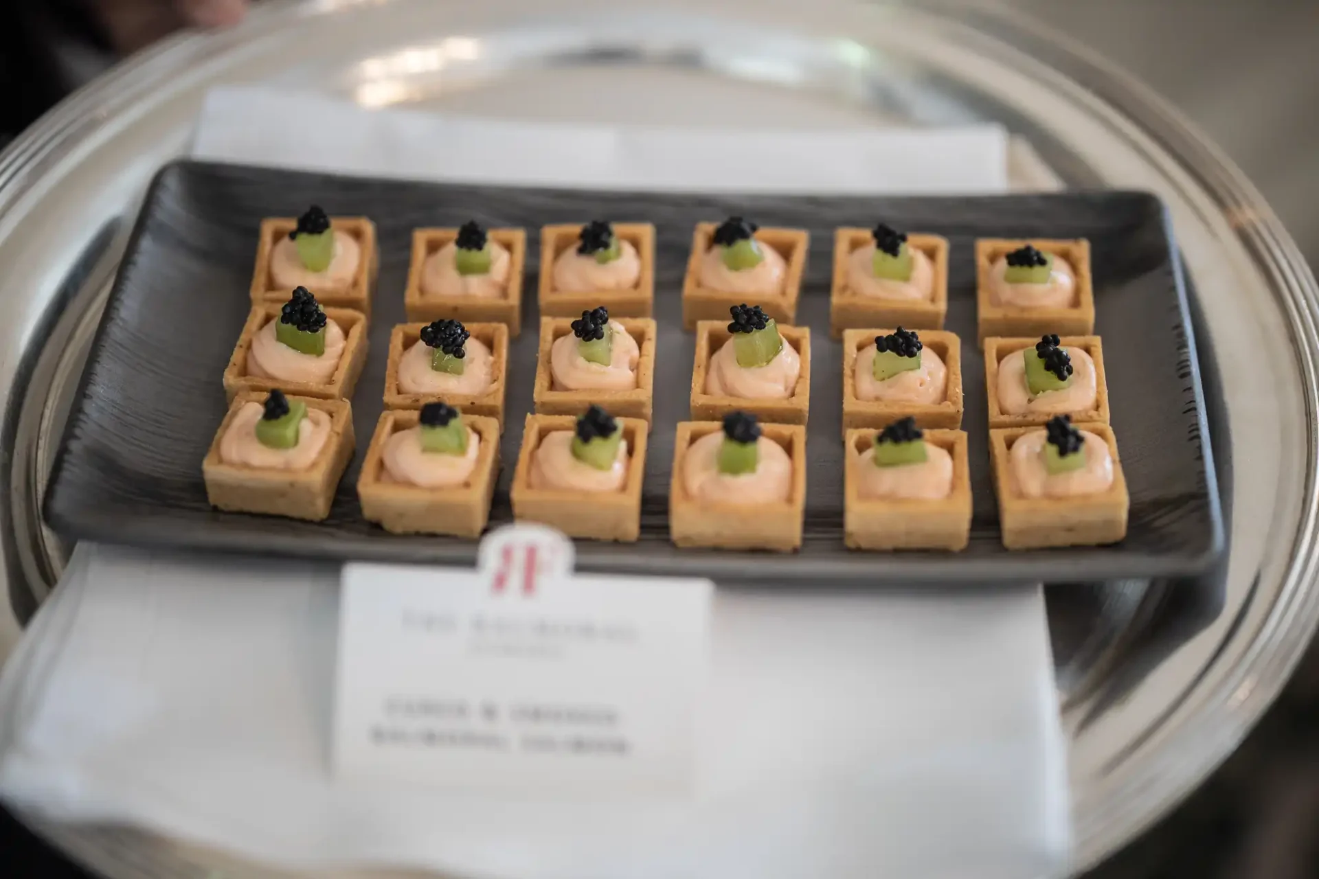 A tray of elegantly presented salmon and caviar appetizers, each garnished with a small leaf, ready to be served at an event.
