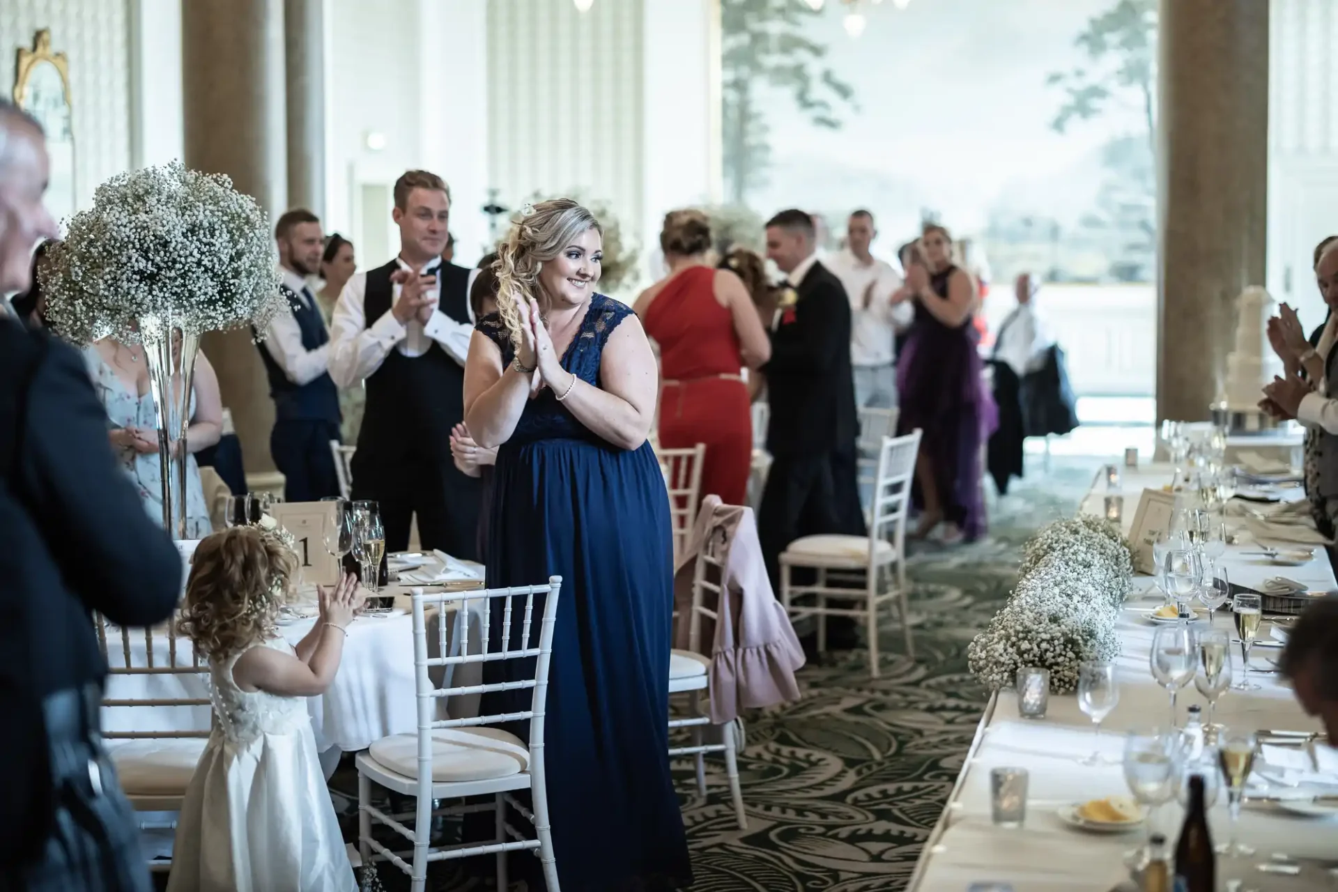 A joyous bride entering a reception hall, clapping guests and elegant tables lined with floral arrangements.