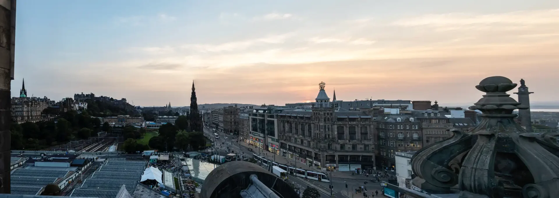 Panoramic view of edinburgh at sunset featuring historic buildings and busy city streets, with edinburgh castle on the left and scott monument visible.