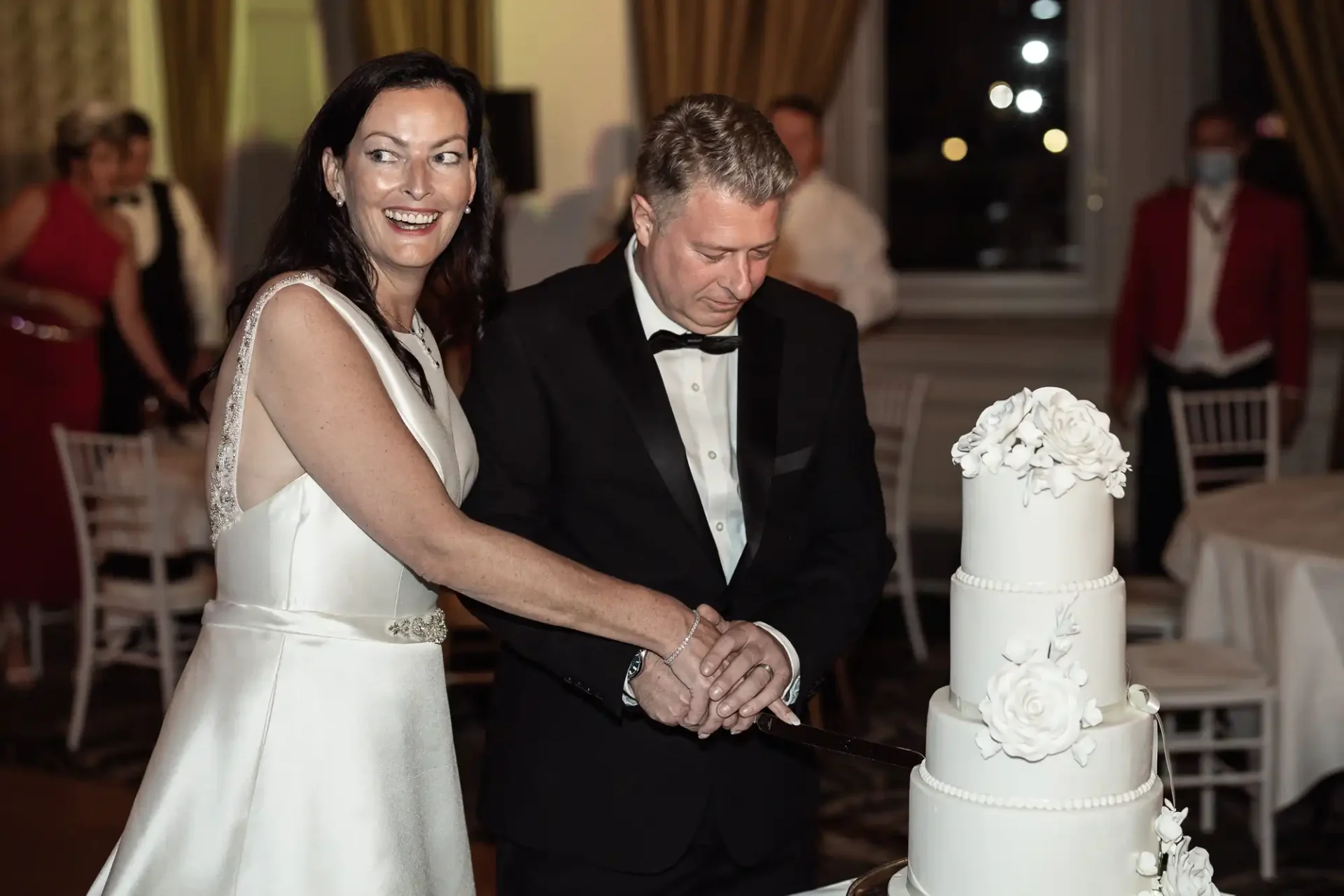 A couple in formal attire cutting a tall white wedding cake adorned with floral decorations.