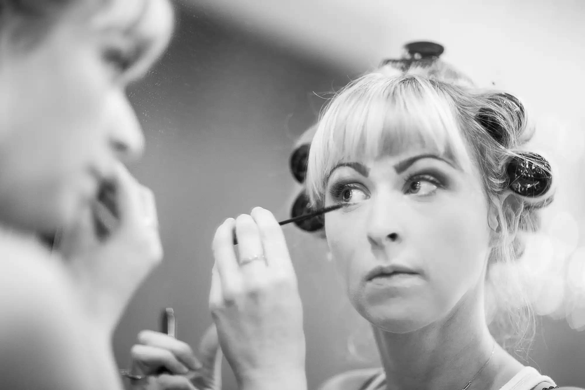 Woman applying mascara, looking in mirror, with hair in rollers. black and white photo.