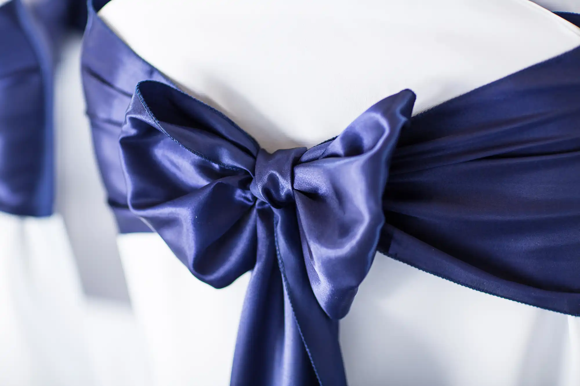 Close-up of a navy blue satin bow on a white chair cover, typically used for elegant event decorations.