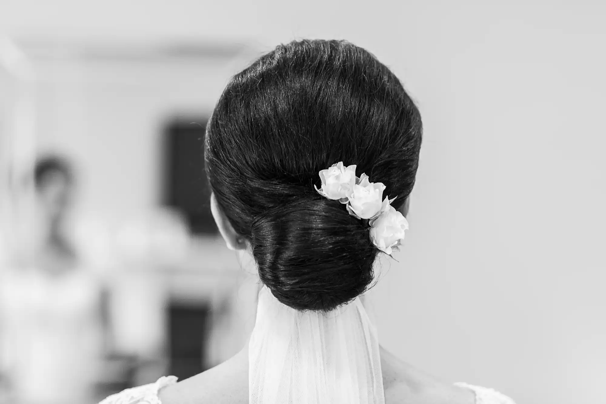 Black and white photo of a woman from behind showing an elegant updo hairstyle with small white flowers.