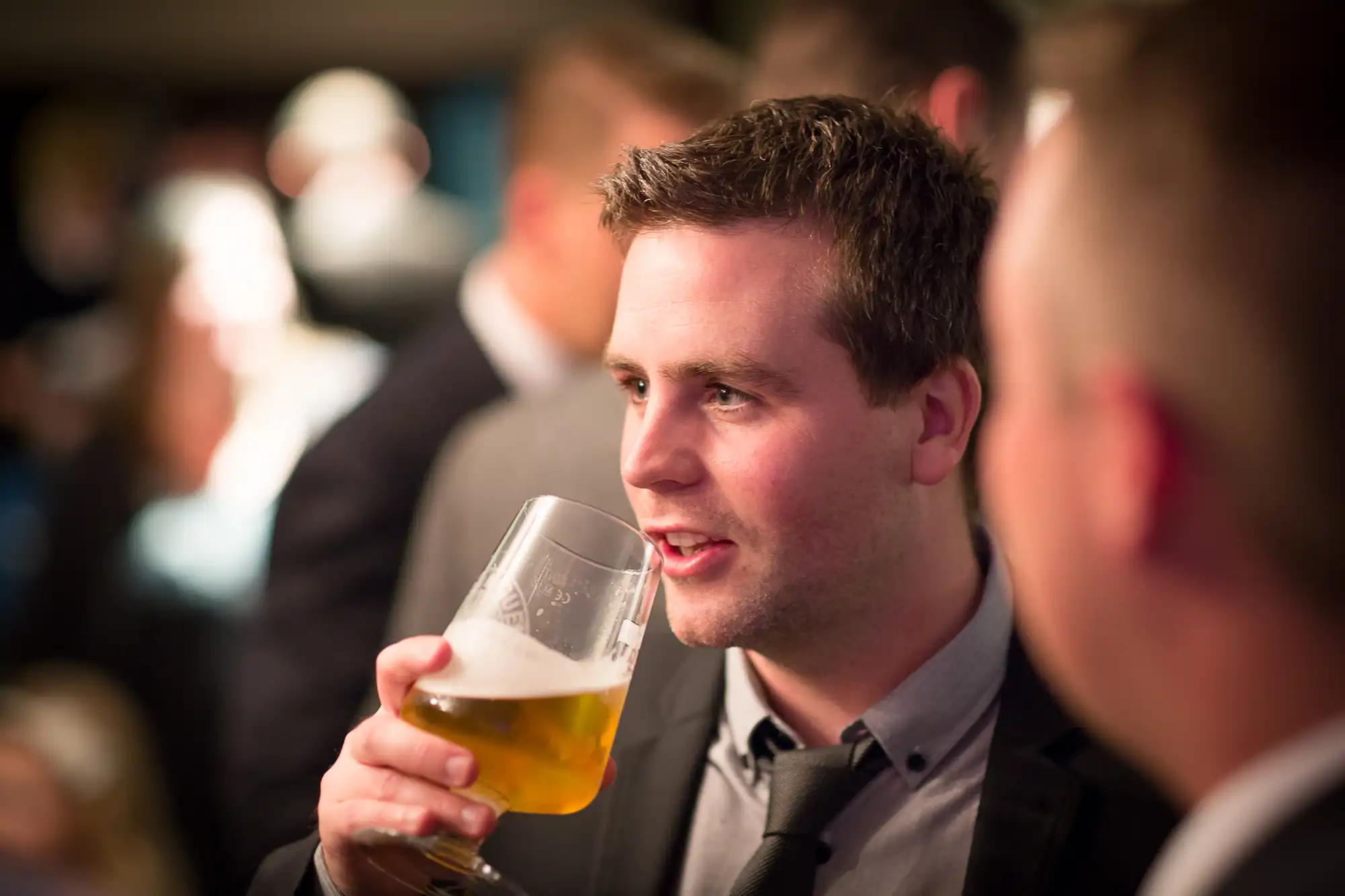 A man in a suit holding a beer glass, engaging in conversation at a social event.