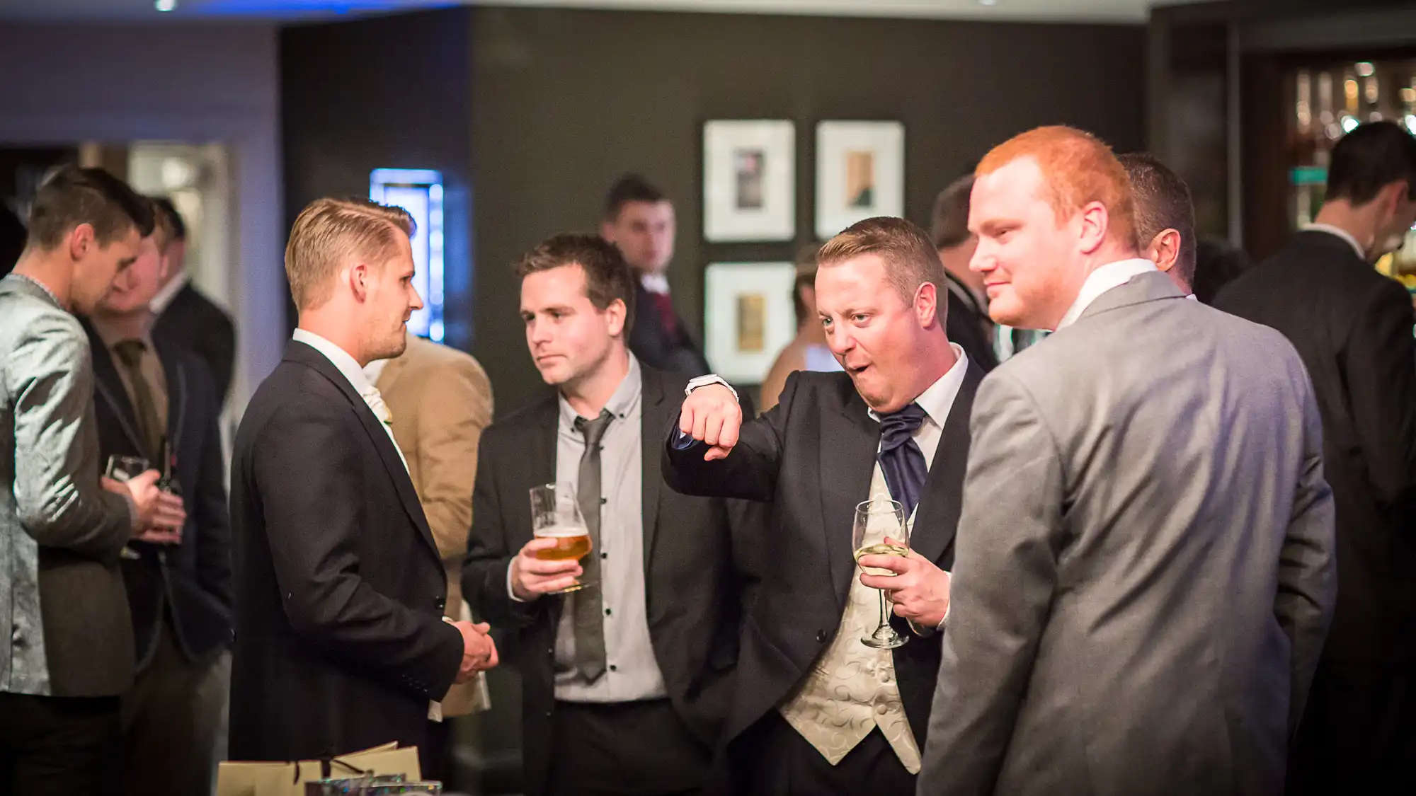Group of men in suits engaged in conversations at a formal event, some holding drinks.