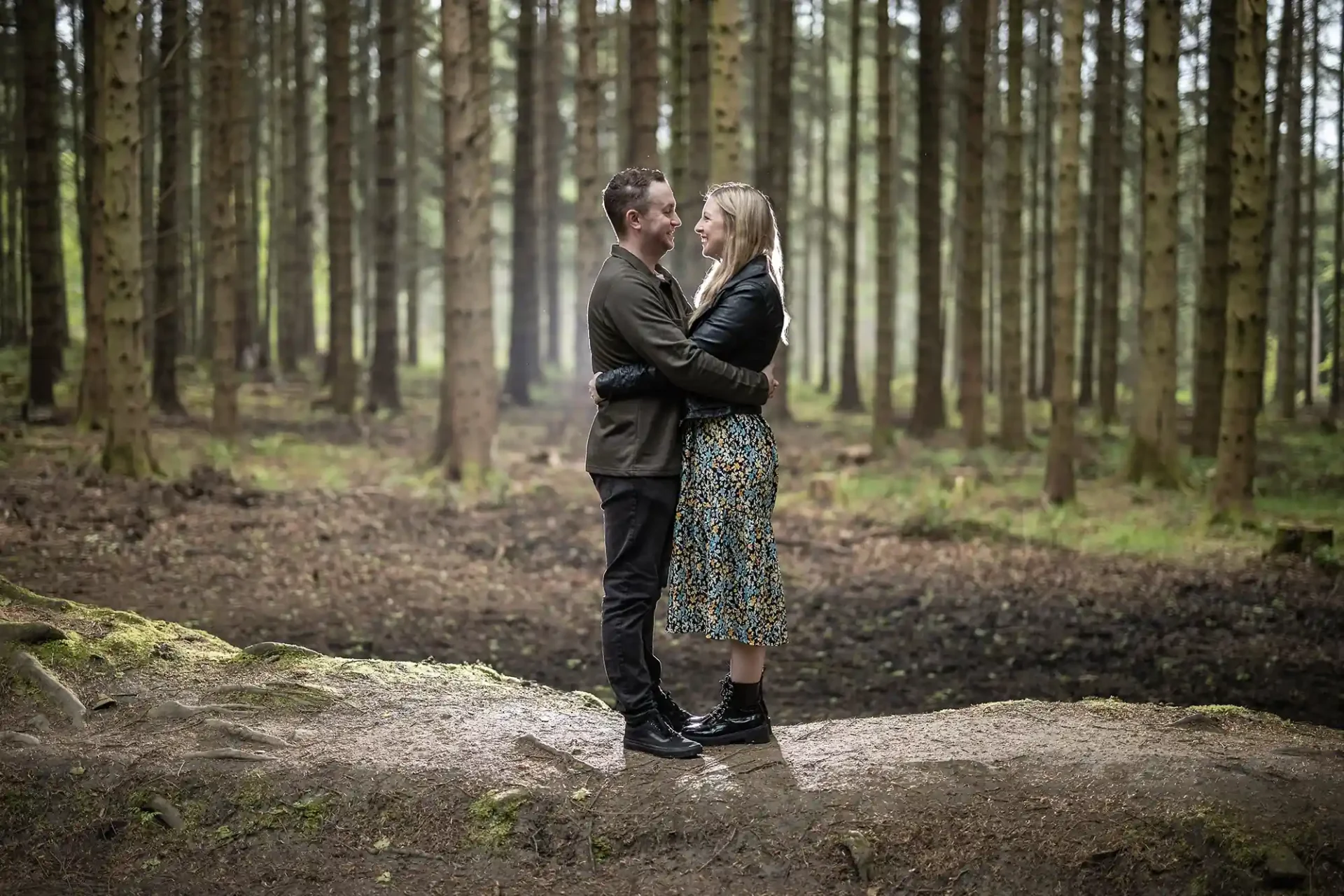 A couple embracing and smiling at each other in a dense, wooded forest.