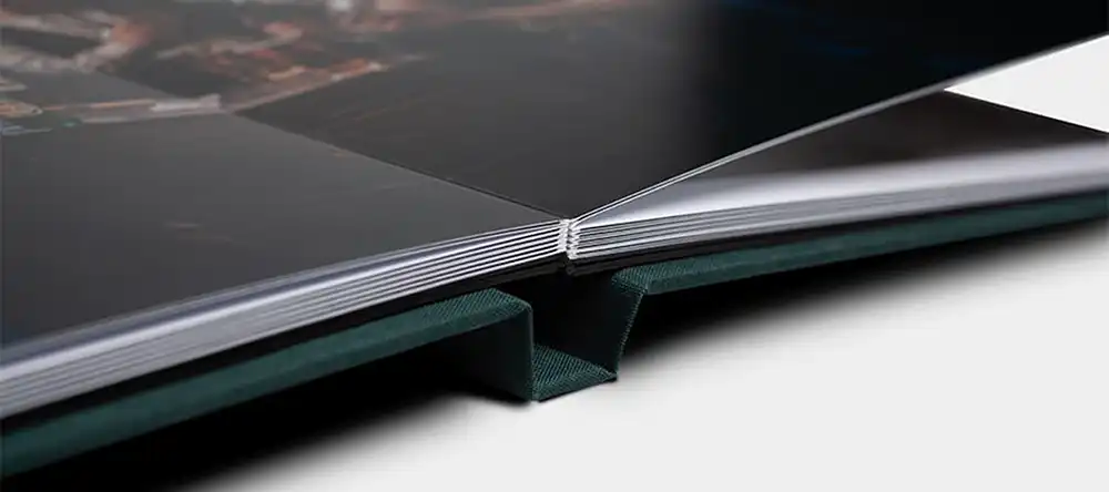 Close-up of an open Bellissimo Perfetto luxury wedding album showing its spine binding and partially visible pages, resting on a flat surface.