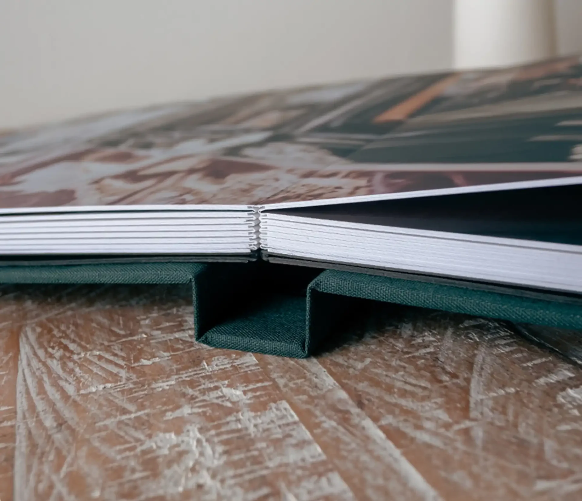 Luxury wedding albums Scotland: Close-up of an open photo book placed on a wooden surface, showing the binding and edges of the pages.