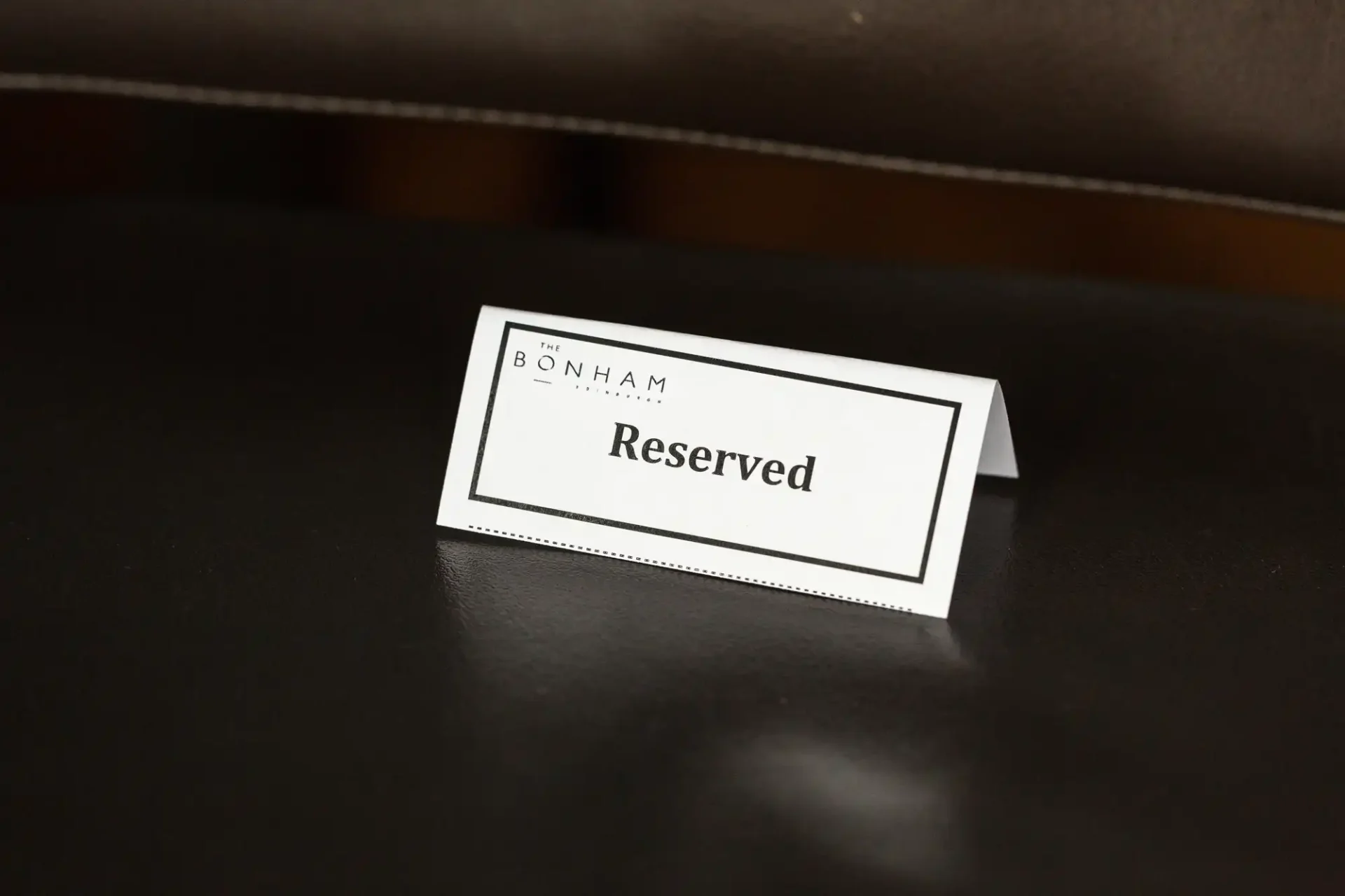 A reserved sign with the text "bonham reserved" placed on a dark, matte surface.