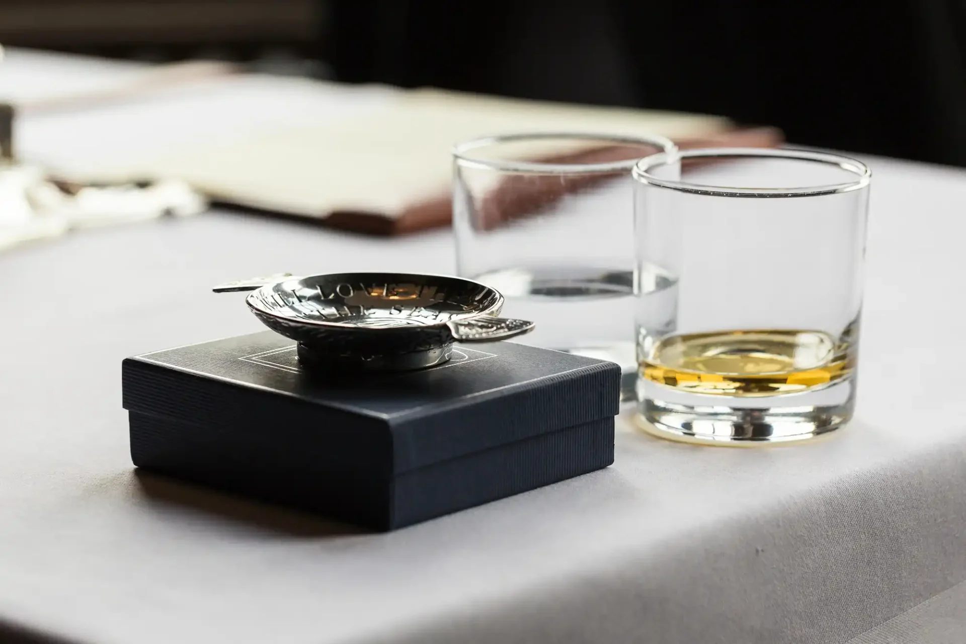 A close-up image of a table setting featuring an ashtray on a small box, and two glasses, one containing whiskey, in a restaurant.