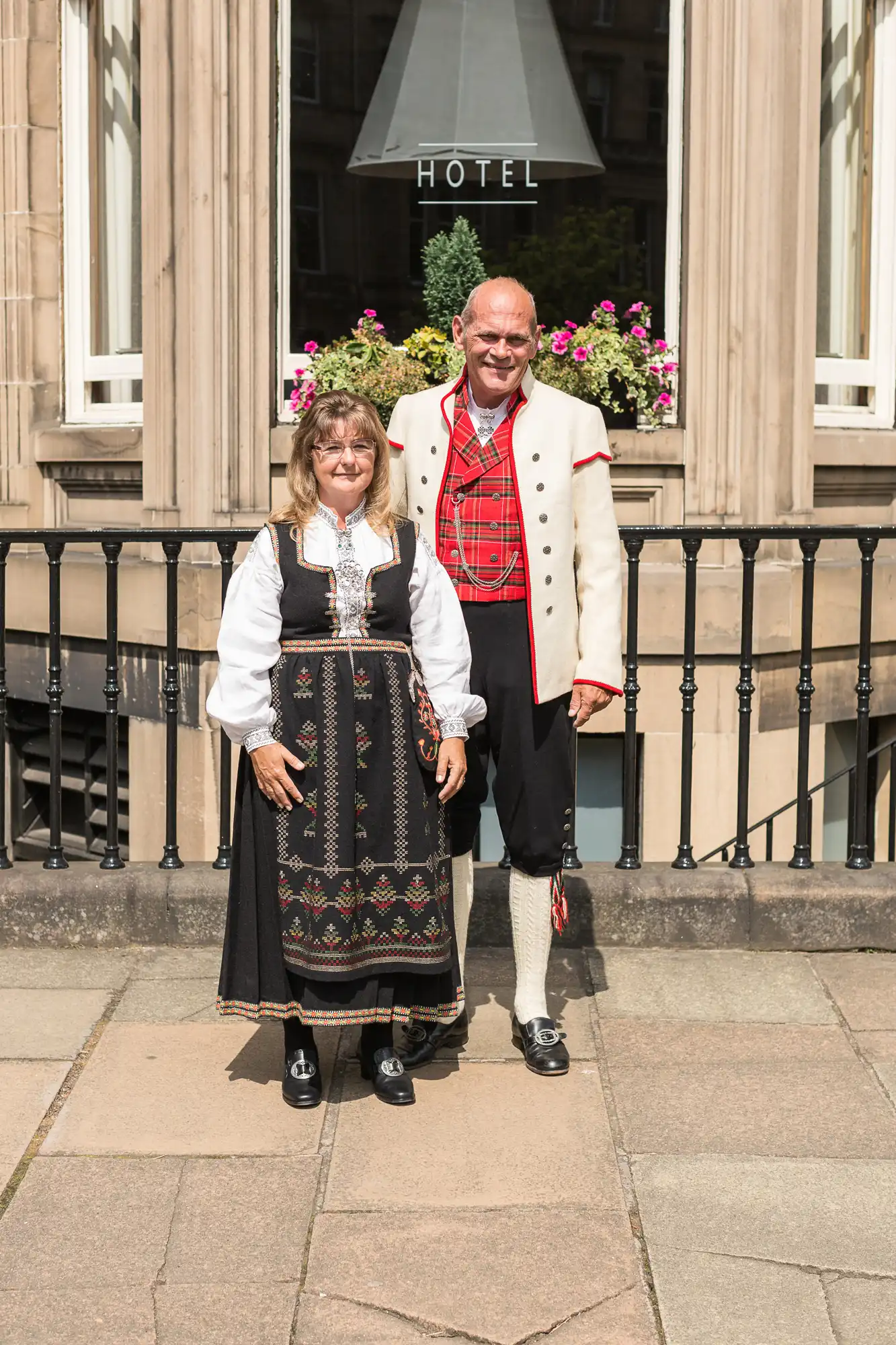A man and a woman wearing traditional norwegian costumes, standing in front of a hotel entrance.