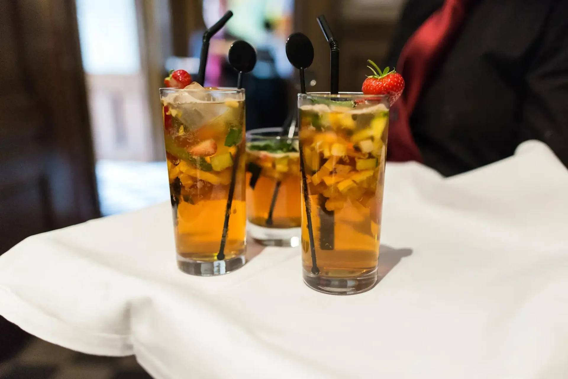 Two glasses of fruit-infused iced tea garnished with strawberries and herbs, served on a white tablecloth.