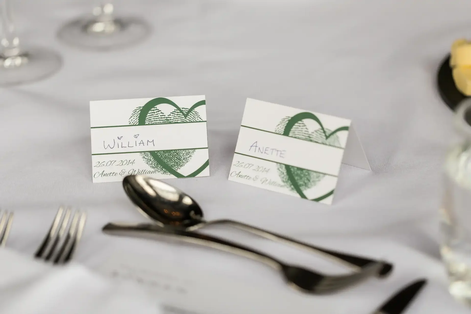Two place cards with the names "william" and "anette" on a white tablecloth at a wedding, flanked by silverware.