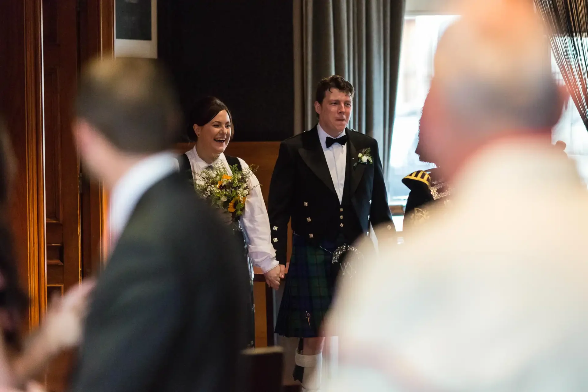 Bride and groom smiling as they walk down the aisle, the bride in a white dress and the groom in a kilt.