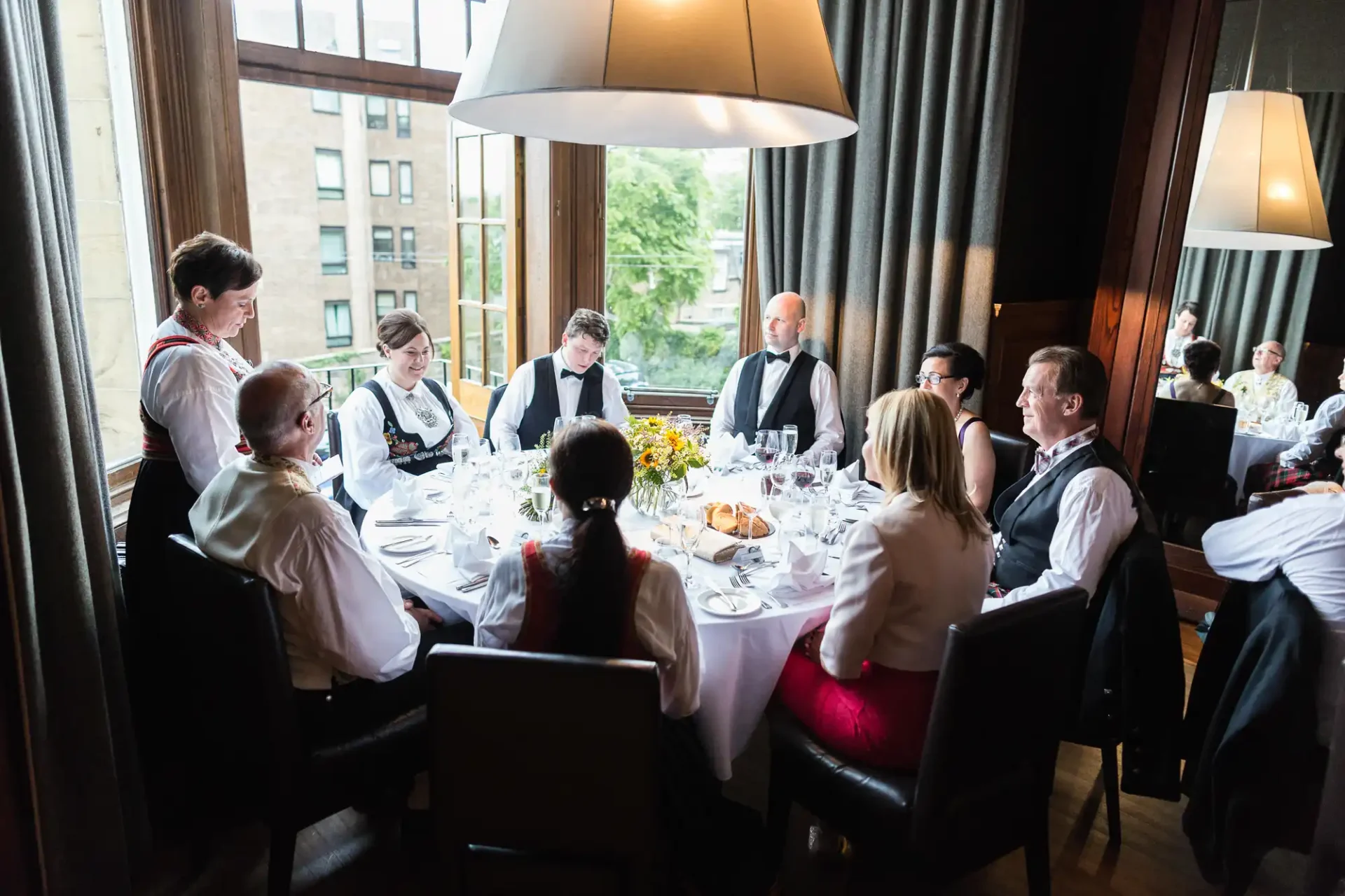 Elegant dining setting with a group of formally dressed adults seated around a table, being attended to by waitstaff in a luxurious restaurant.