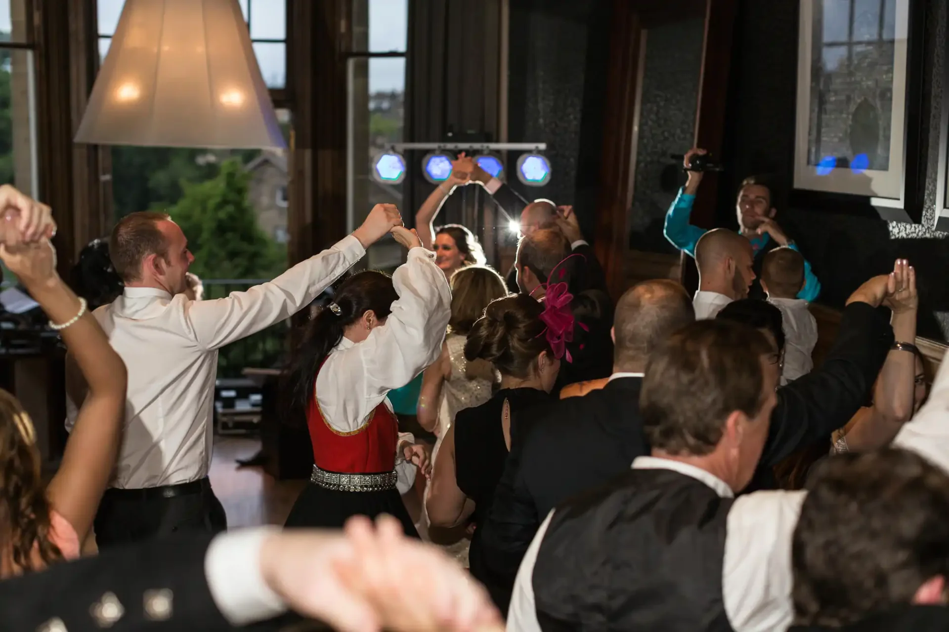 Guests dancing and celebrating enthusiastically at a lively indoor wedding reception, with focus on a joyful bride and groom in the center.