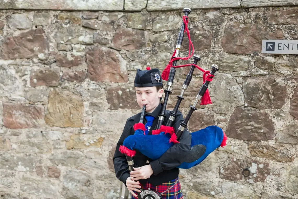 Young boy playing the bagpipes in front of stone wall