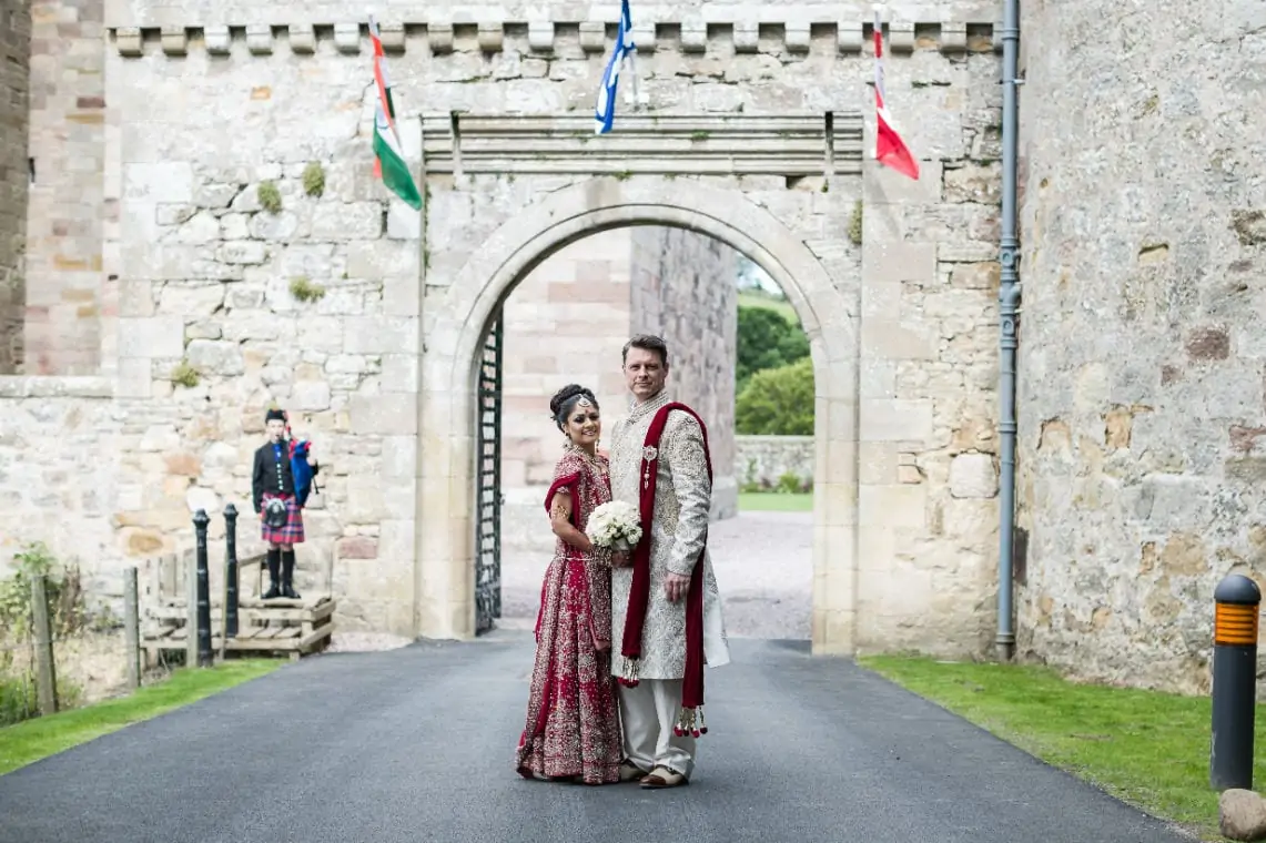 Newlyweds standing outside the arch entrance to the castle