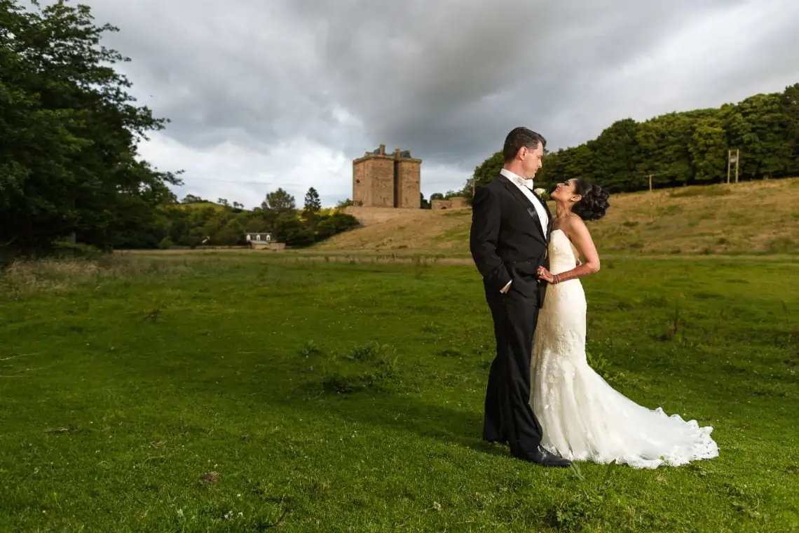 Newlyweds looking at each other standing in a field with the castle in the distance