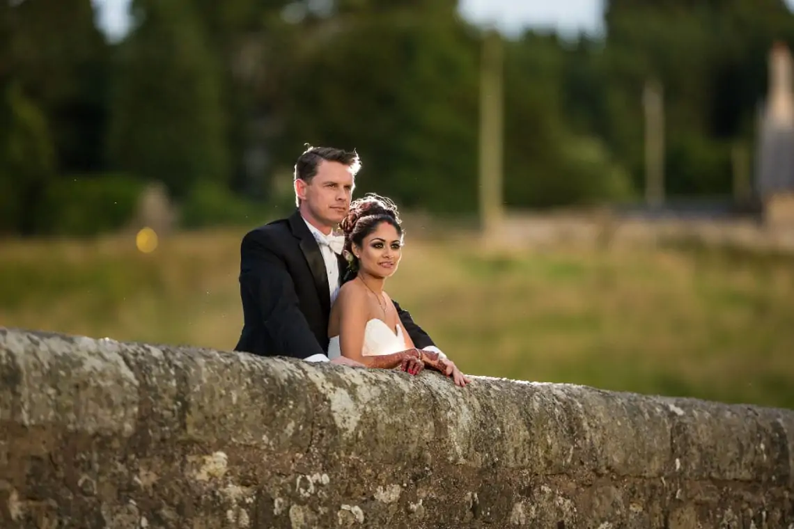Newlyweds standing on an old picturesque stone bridge