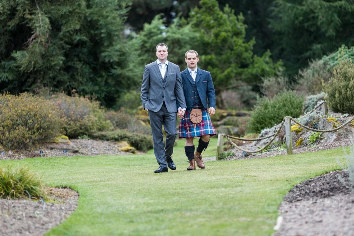 Botanic Gardens same-sex newlyweds holding hands walking across the grass looking at camera