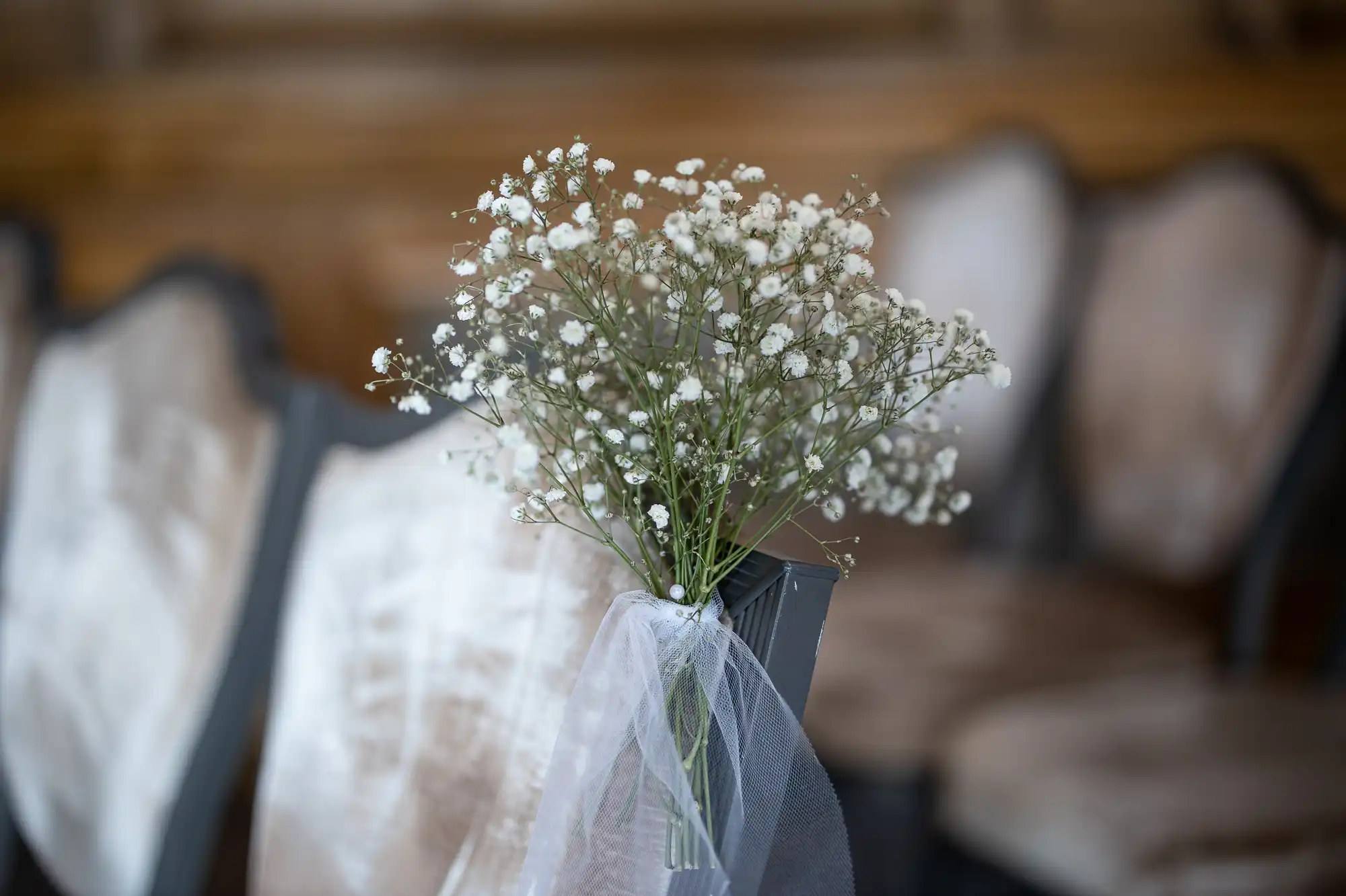 A bouquet of baby's breath flowers attached to a chair with a white ribbon in a rustic indoor setting.