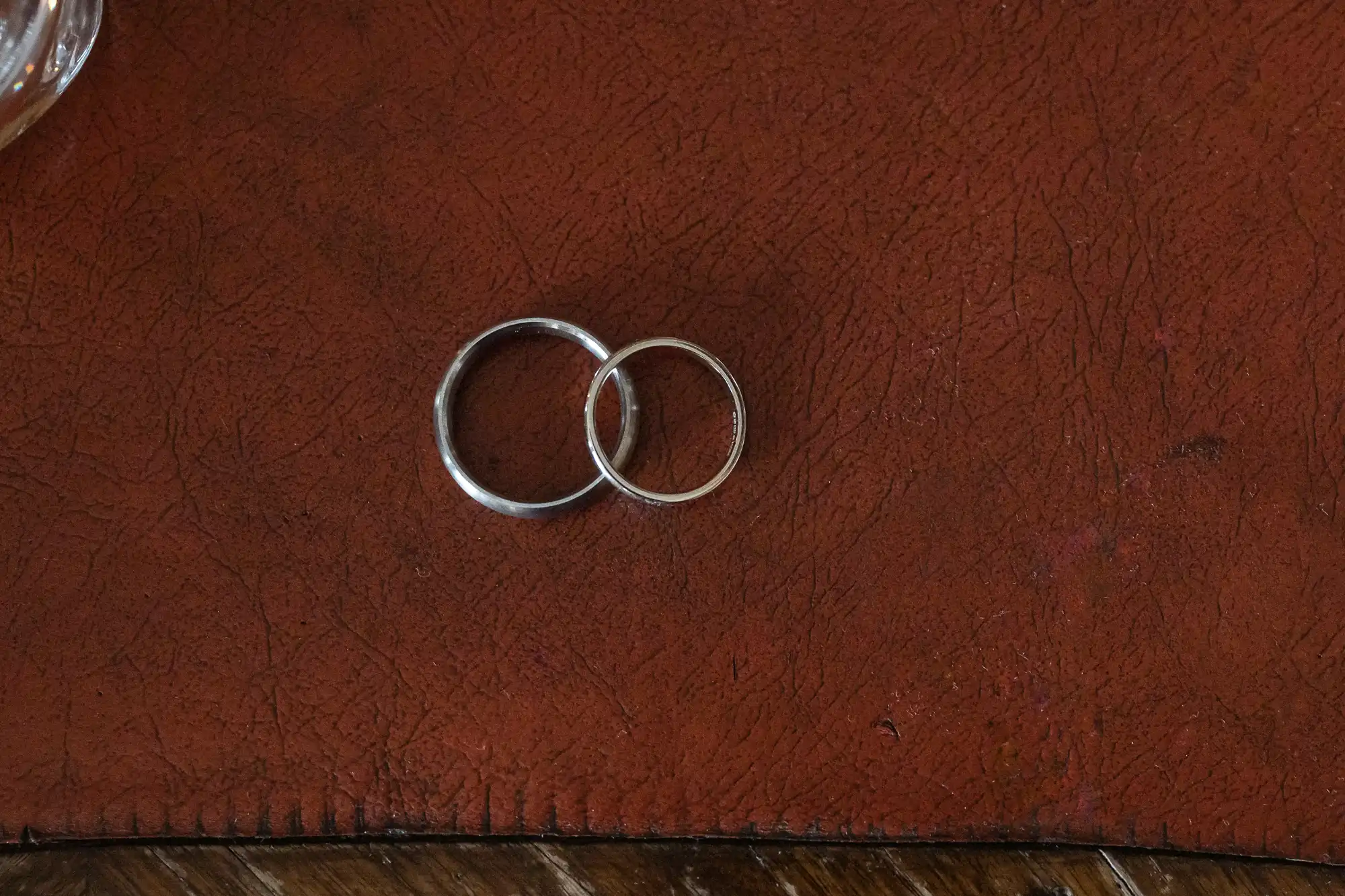 Two wedding rings lie closely together on a textured, reddish-brown leather surface.