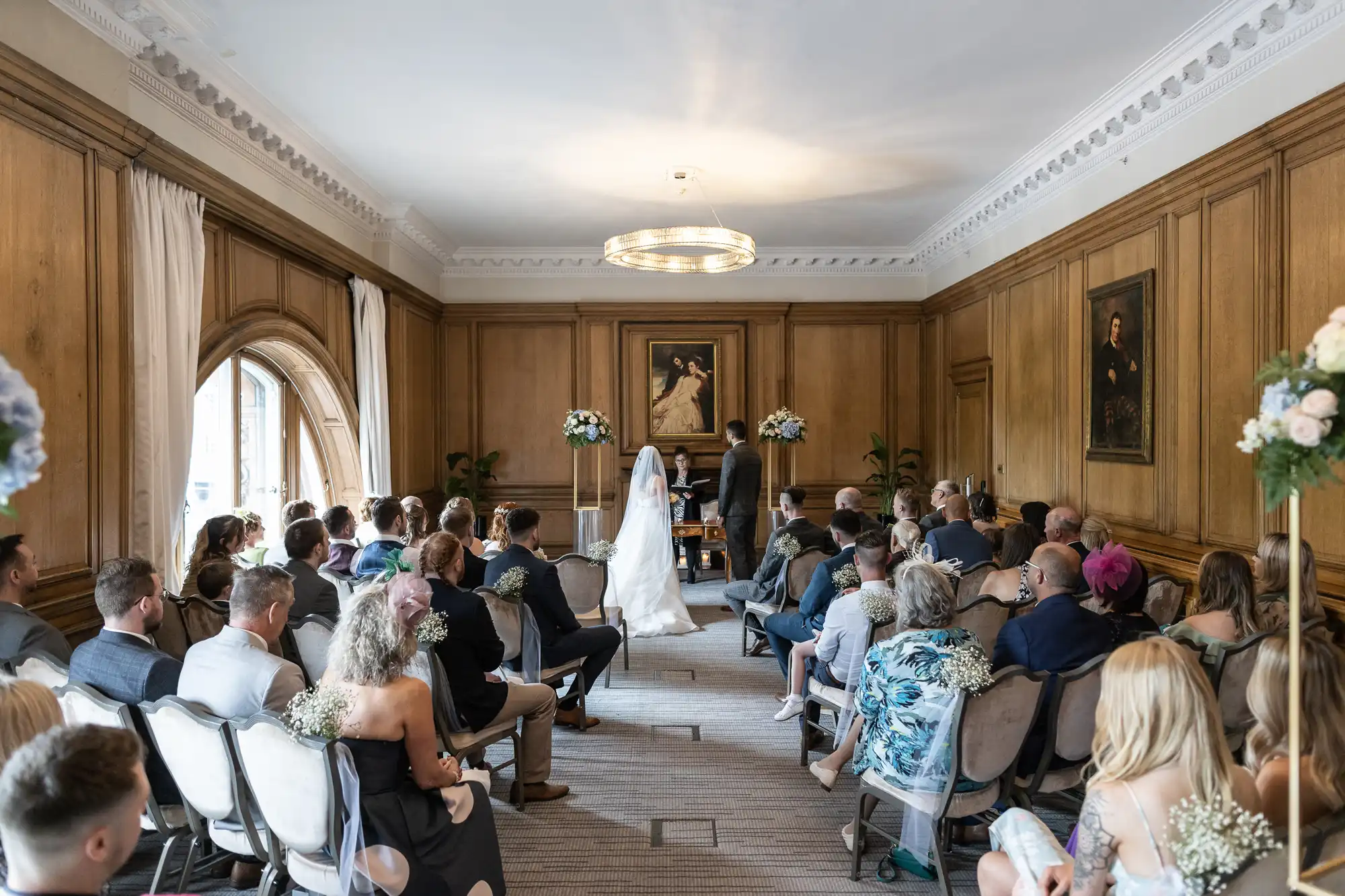 A wedding ceremony in an elegant room with guests seated as a couple stands in front of the officiant.