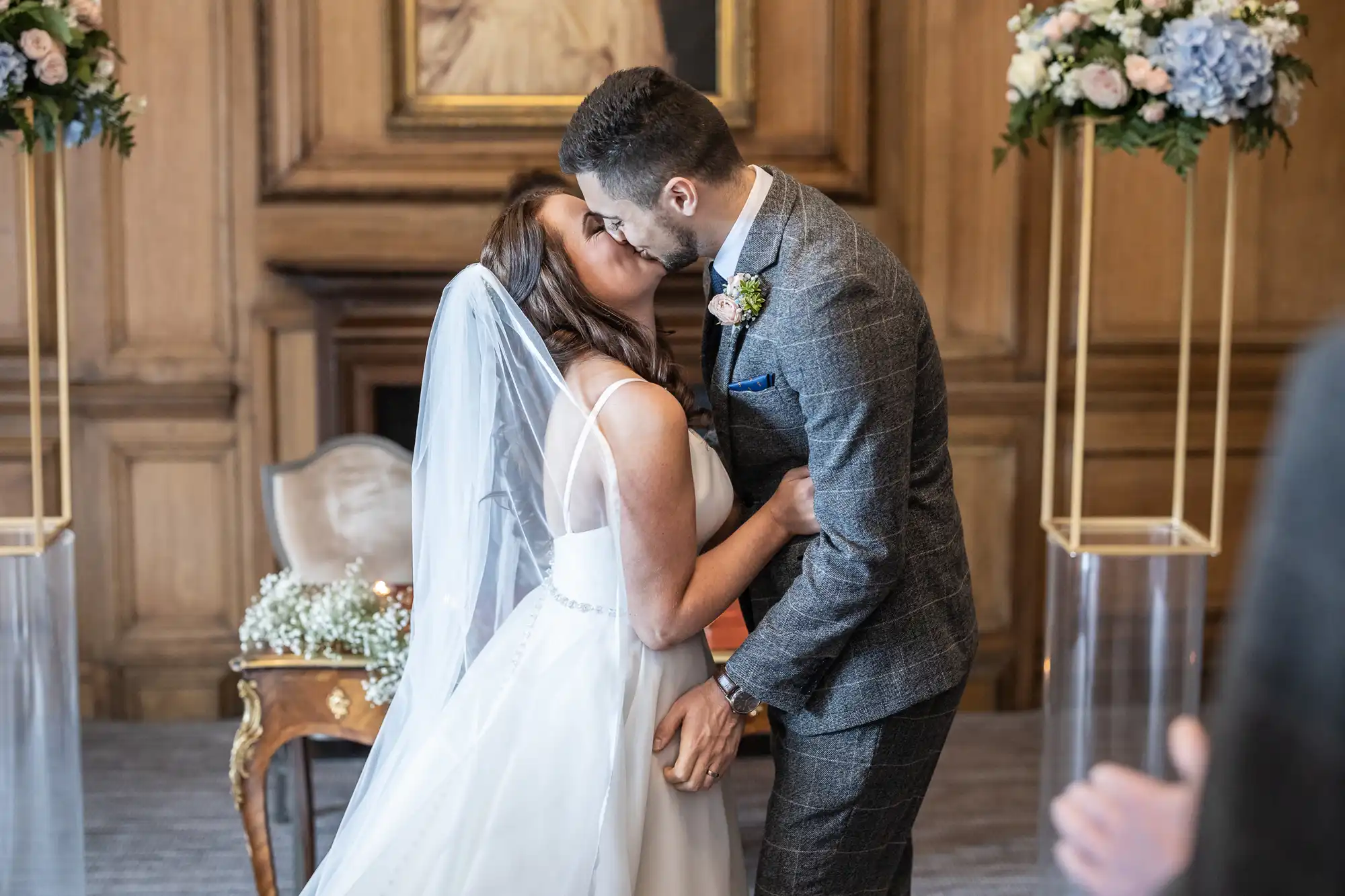 A newlywed couple kissing passionately inside a beautifully decorated room with floral arrangements.