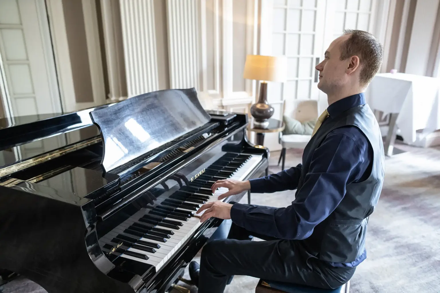 A man playing a grand piano in a well-lit, elegant room.