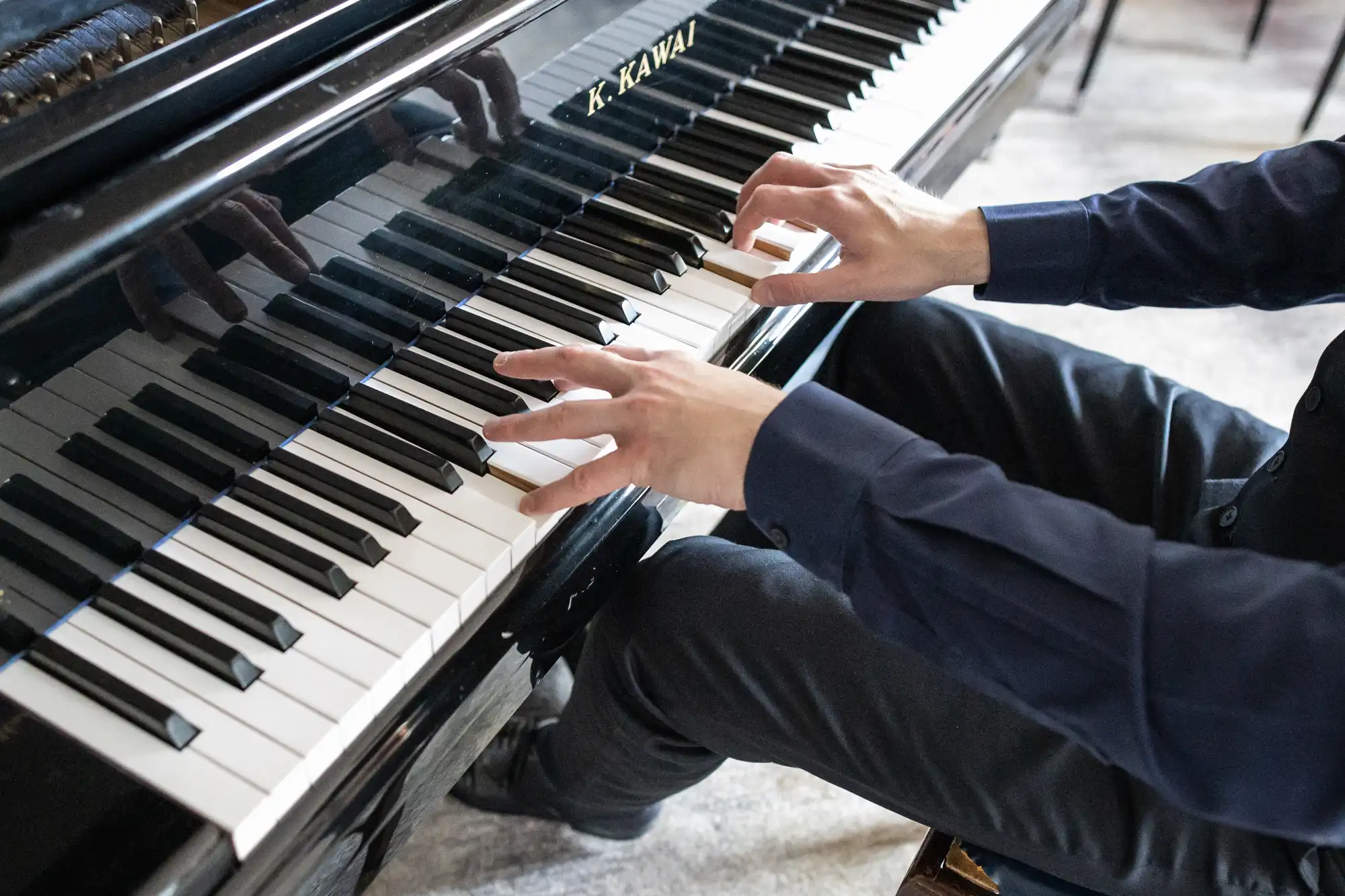 A person playing a Kawai grand piano, focusing on their hands as they press the black and white keys.