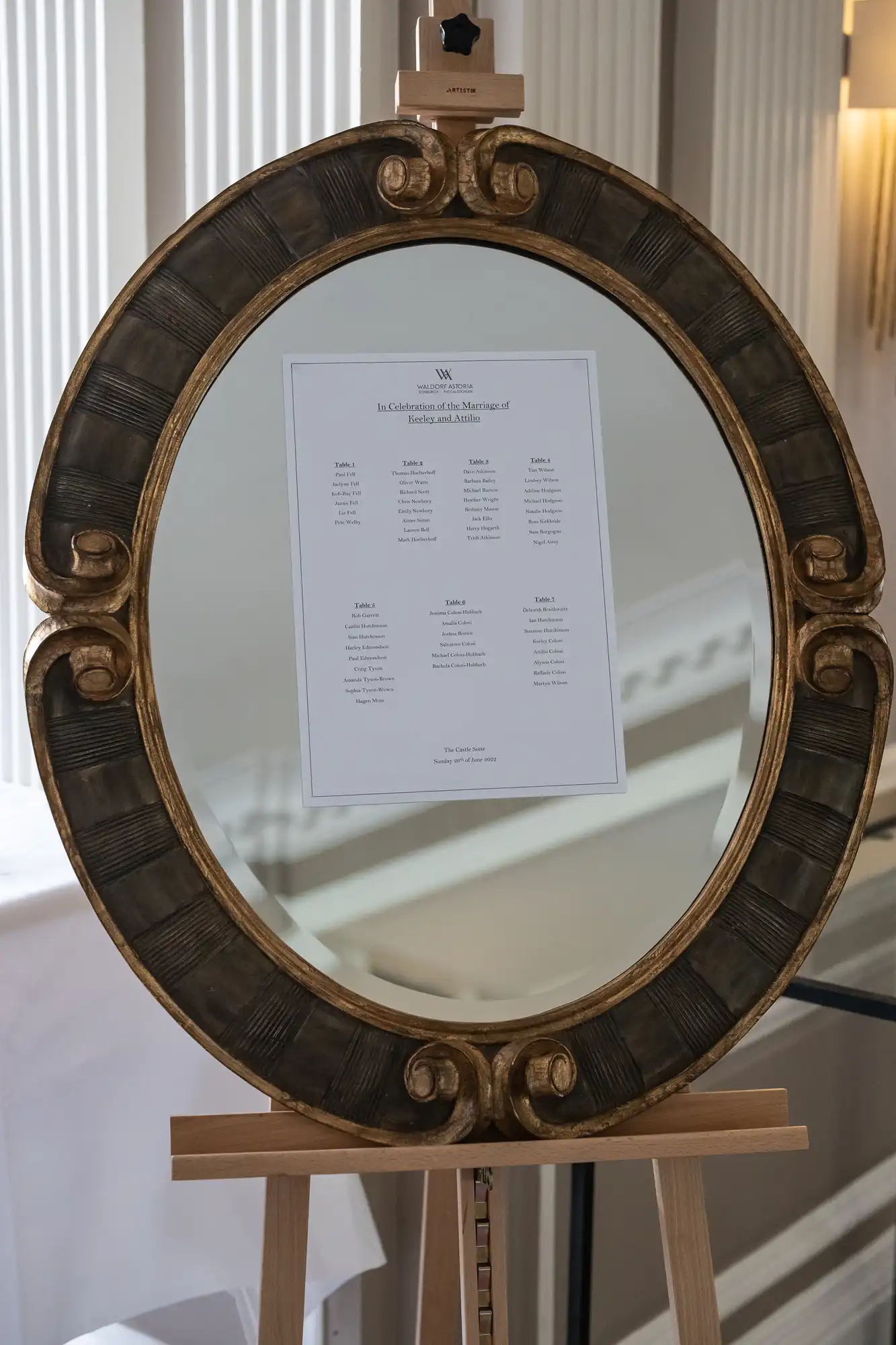 An ornate oval gold frame on an easel displaying a menu, situated in an elegant room with soft lighting.