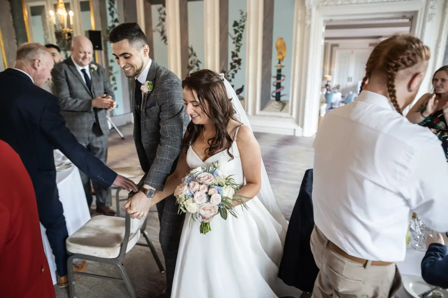 A bride and groom greeting guests in an ornately decorated room during their wedding reception.