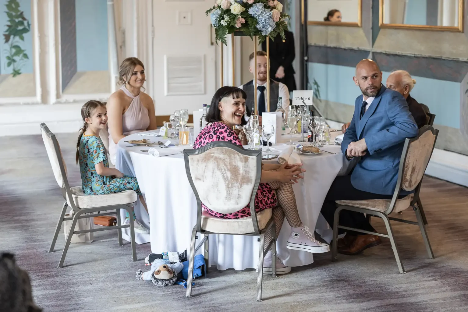 A group of adults and a child seated at a wedding reception table, smiling and engaging in conversation.