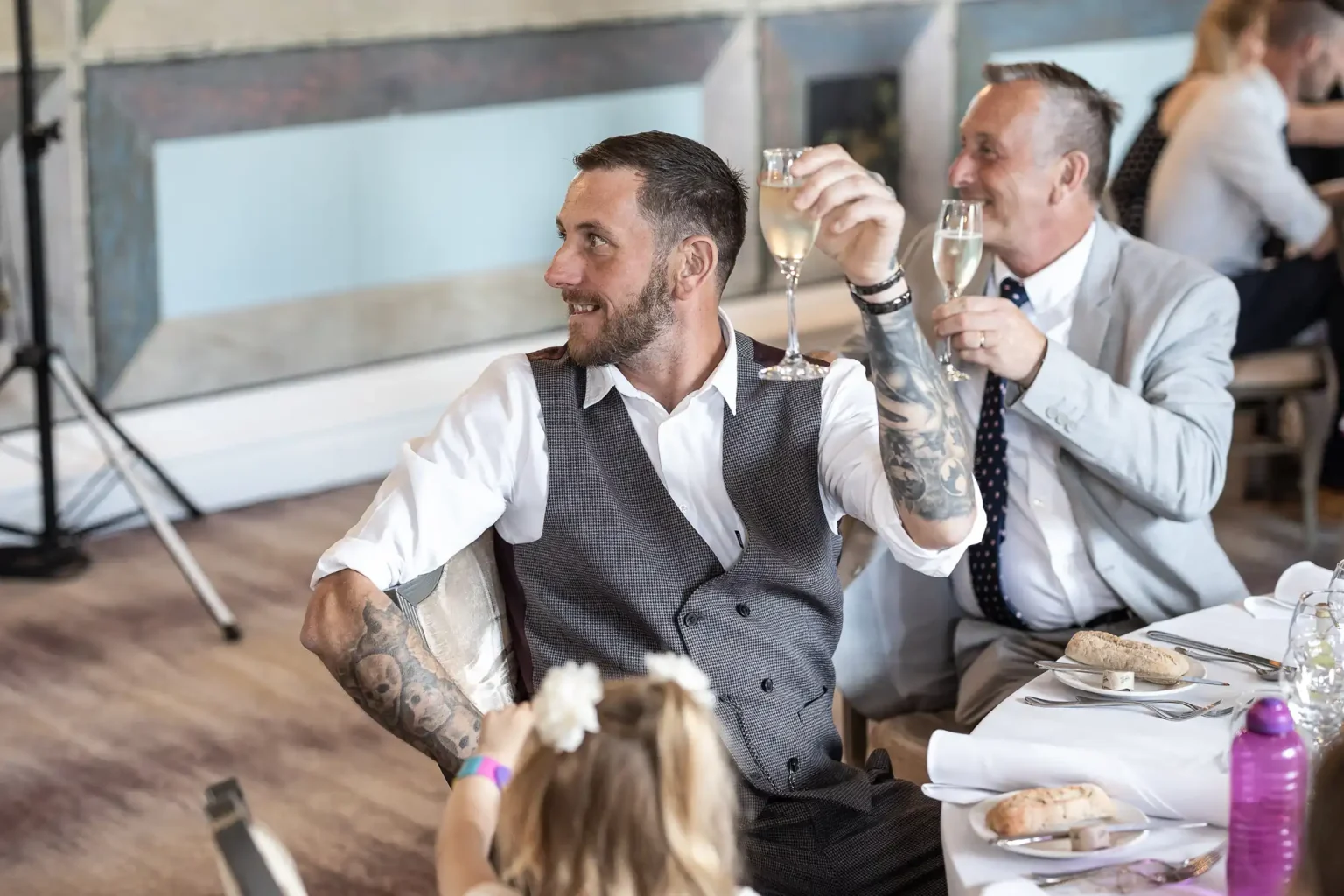 Two men in formal attire raising glasses at a dinner event, smiling and engaging in conversation, with a blurred background emphasizing the festive atmosphere.