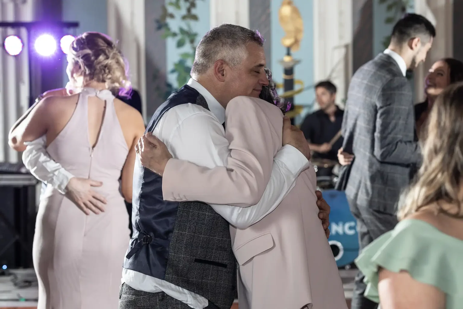 A man and a woman in formal attire sharing a heartfelt embrace at a lively indoor celebration.