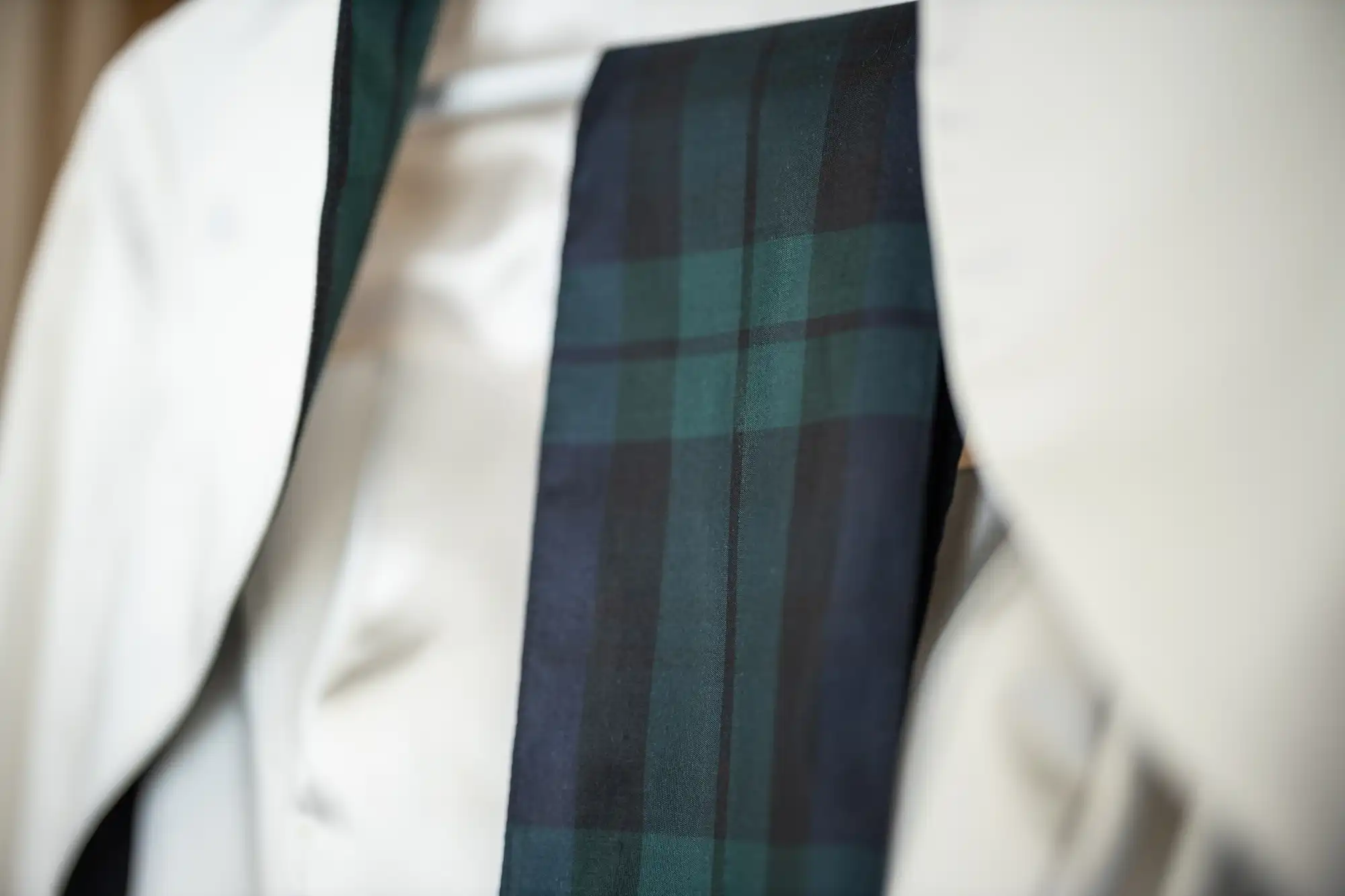 A close-up of a black and green plaid necktie on a white shirt with a jacket draped over the shoulders.