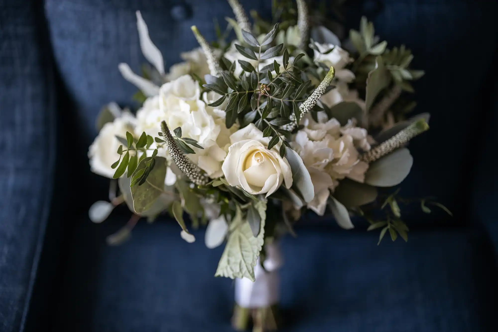 A bridal bouquet of white roses and greenery, set against a dark blue background.