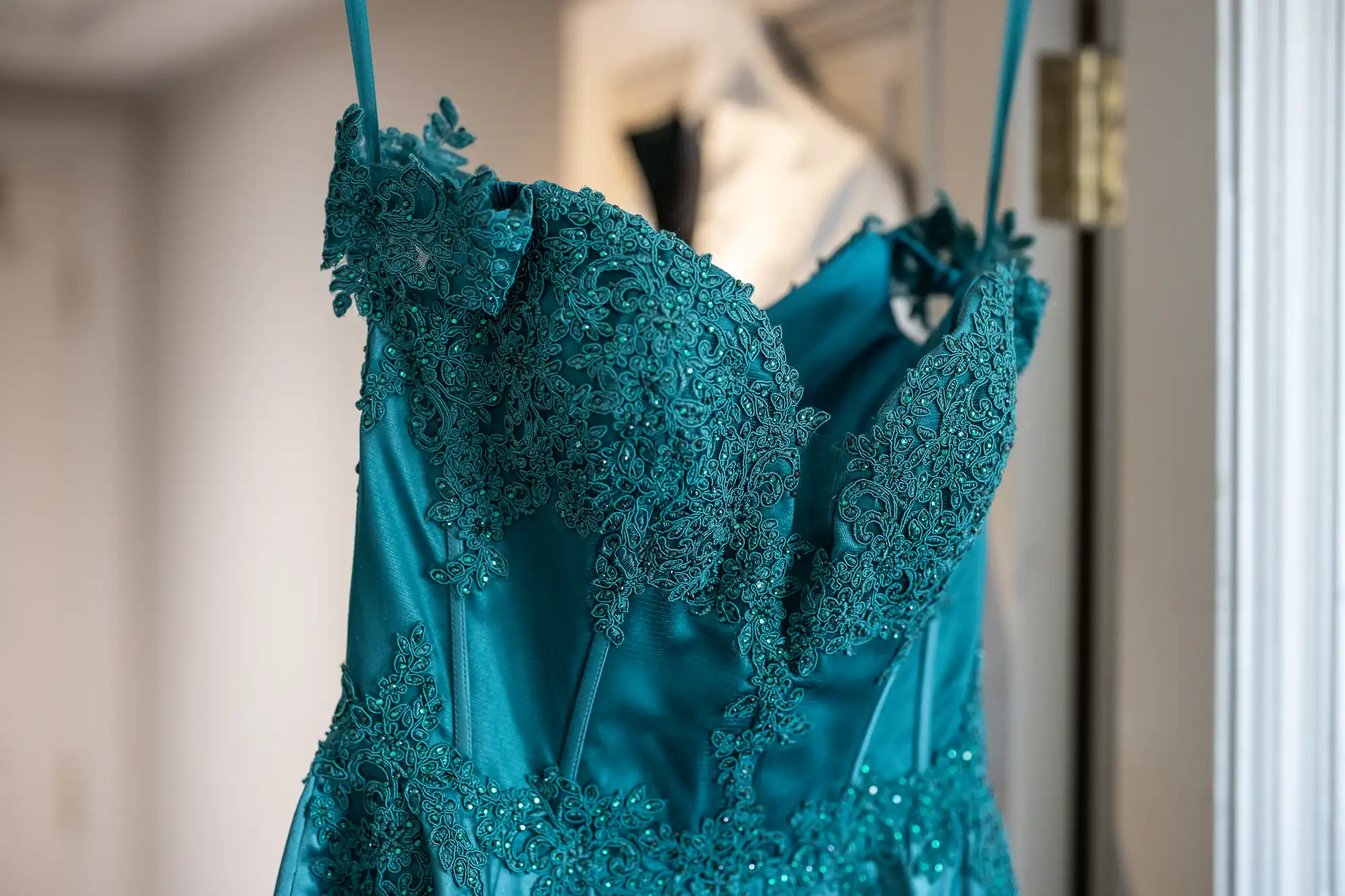 Emerald green lace and satin dress on a hanger, featuring intricate floral lace detailing on the bodice and thin straps.