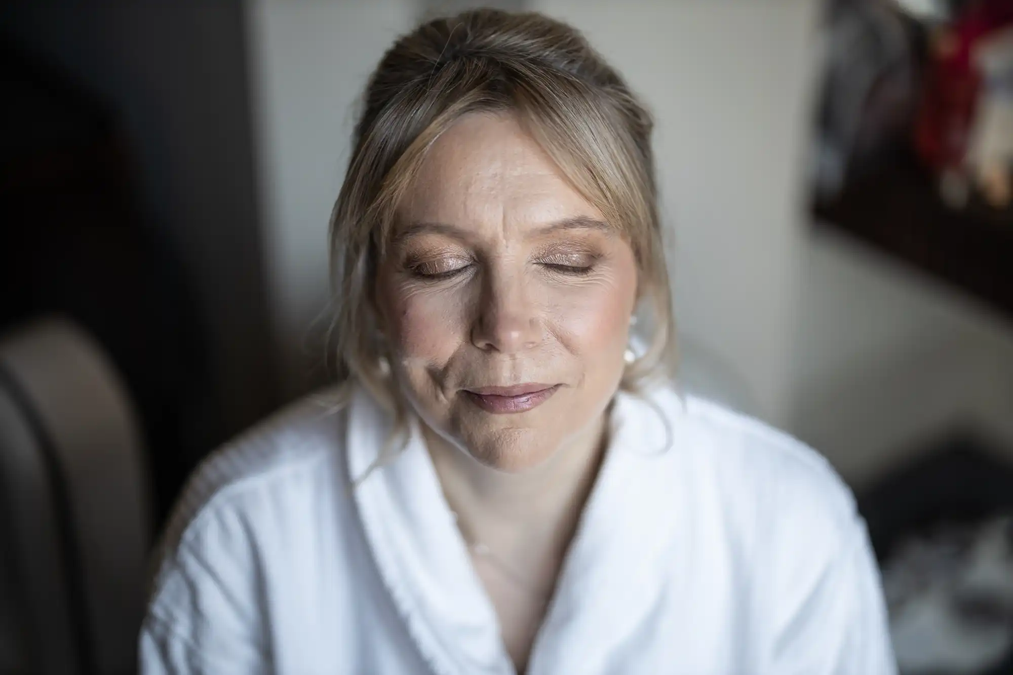 A woman with closed eyes, wearing a white robe, appears to be in a relaxed state.