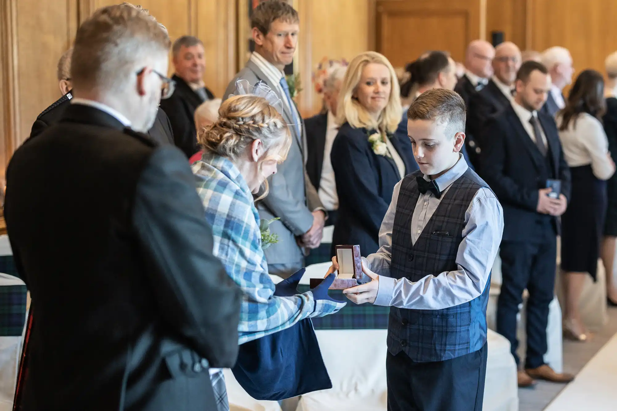 A young boy in a bow tie receives an award from a woman in front of a gathered audience in a formal indoor setting.