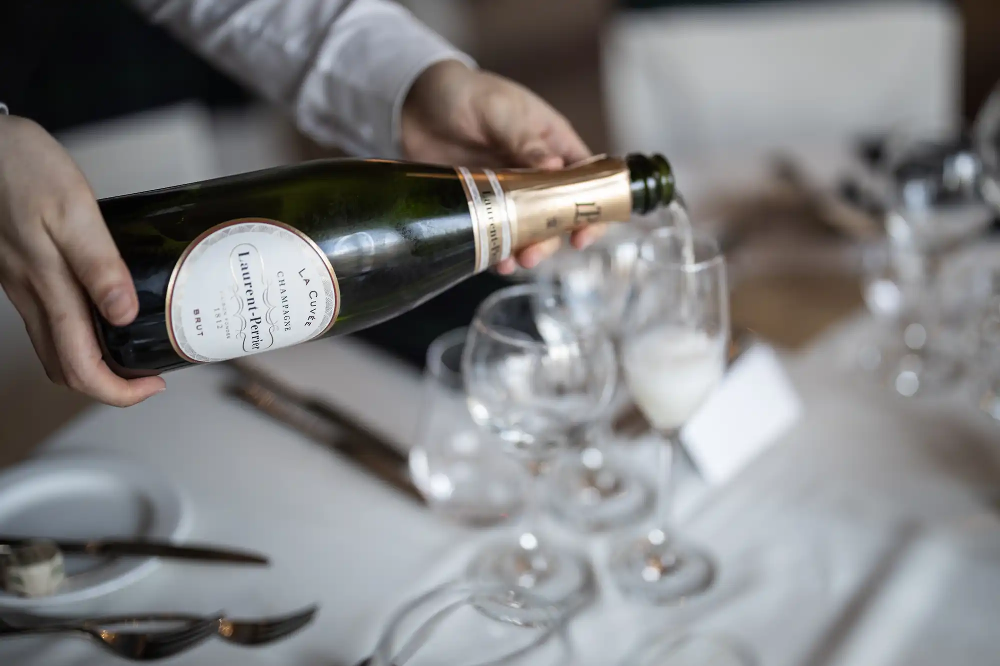 A person is pouring sparkling wine into a glass on a set dining table.