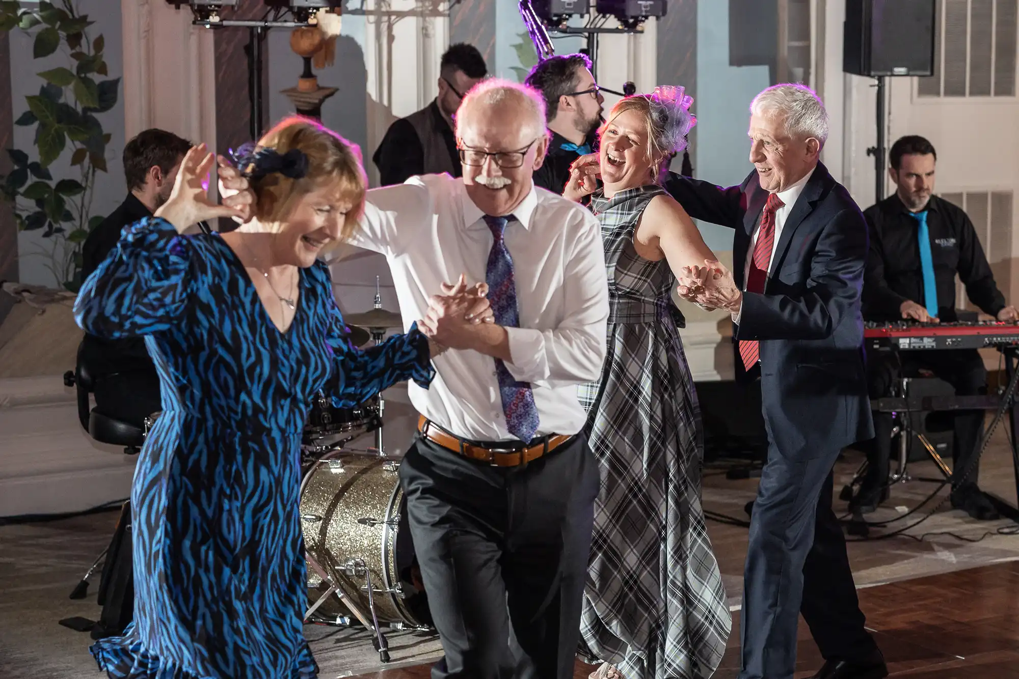 A group of people, dressed in formal attire, dance energetically in front of a live band at an indoor event.