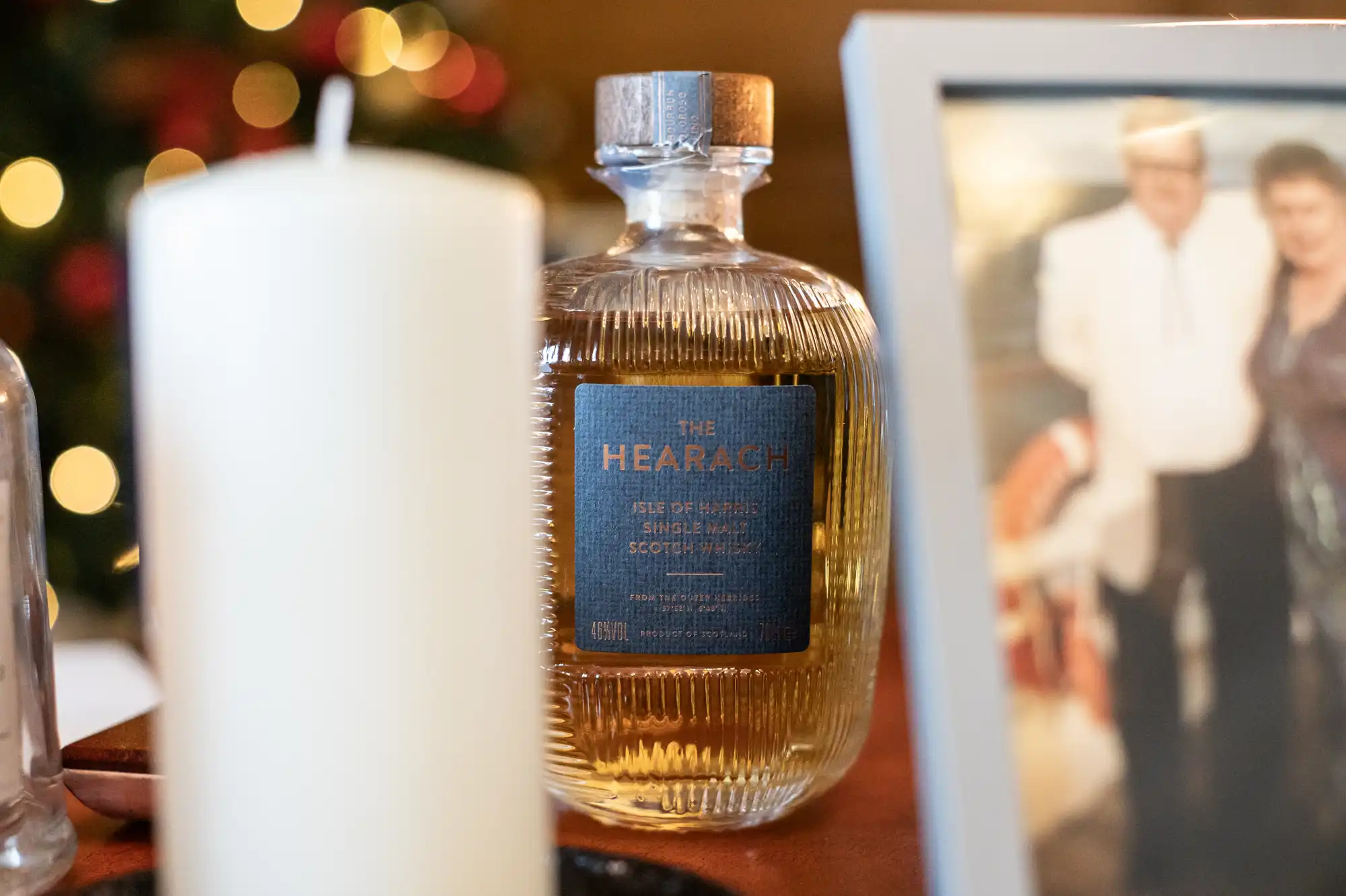 A bottle of The Hearach Isle of Harris Single Malt Scotch Whisky sits on a table next to a framed photo and a white candle.