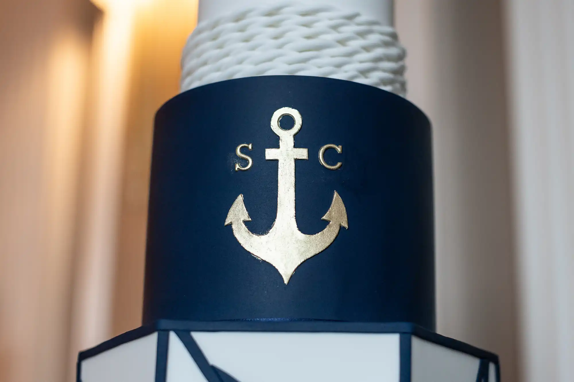 Close-up of a cake decorated with a blue band displaying a gold anchor and the initials "S" and "C". The cake appears to be nautical-themed.