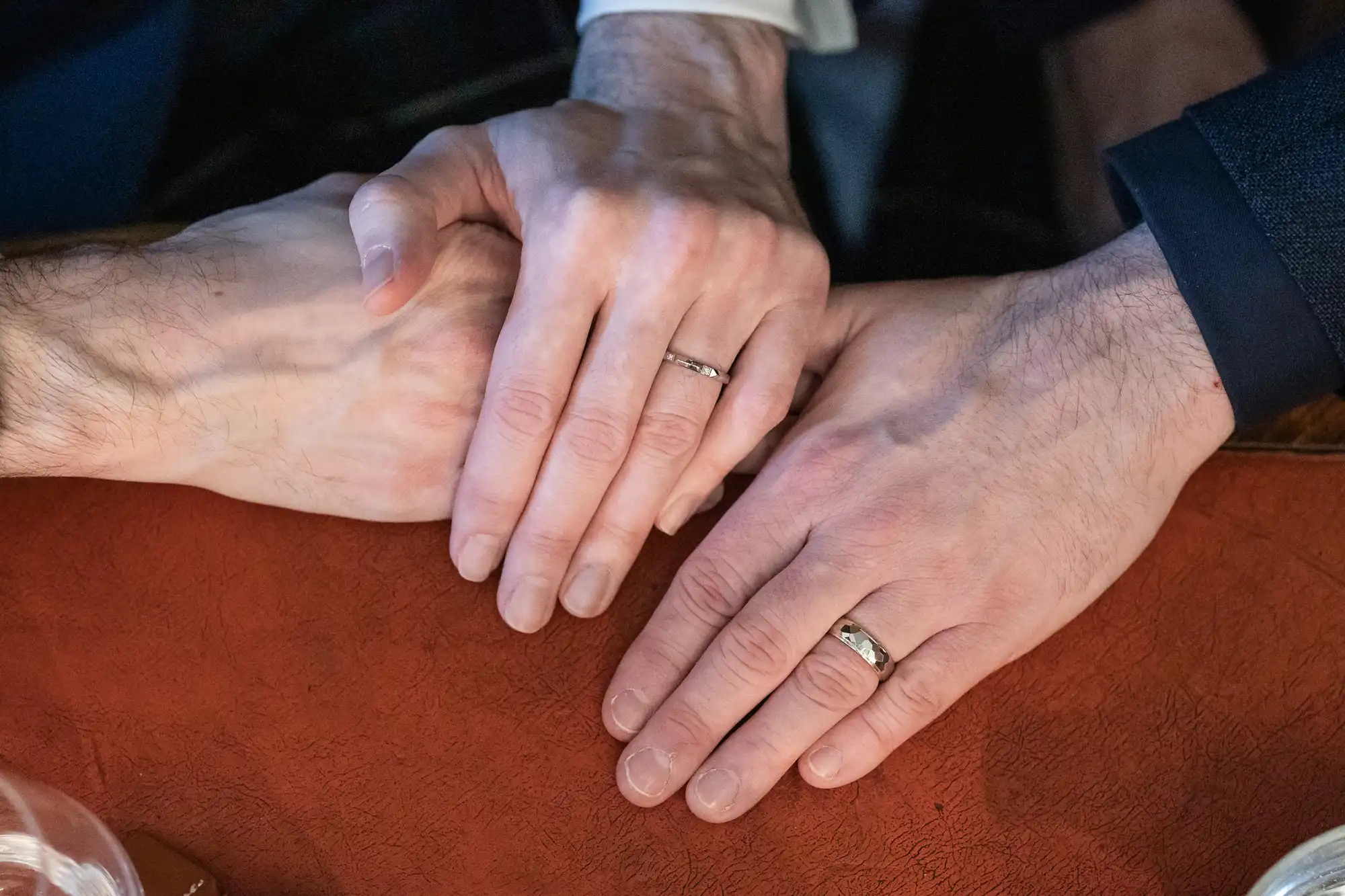 Two people holding hands on a table. Both are wearing wedding bands.