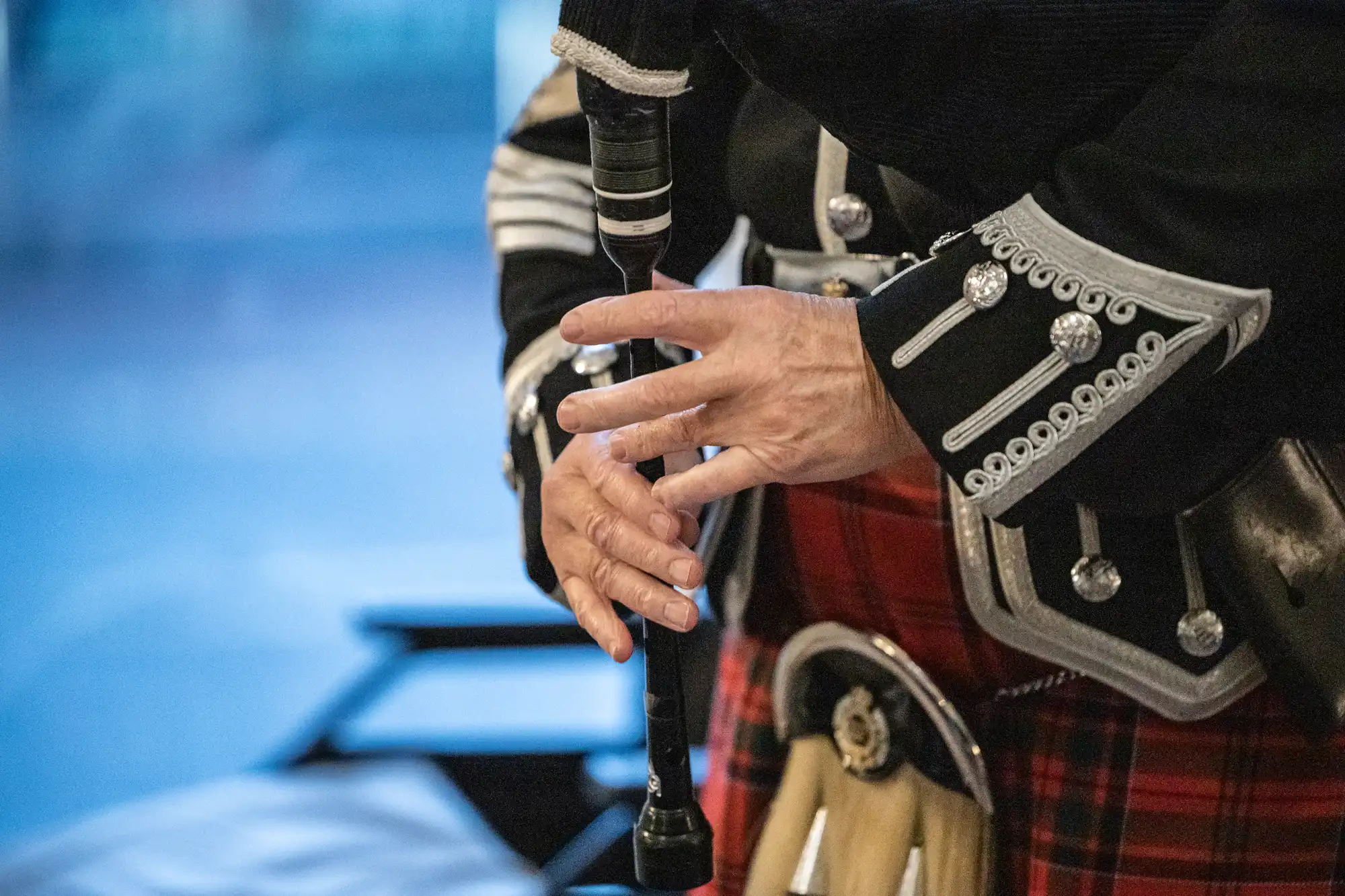Close-up of a person in traditional Scottish attire playing the bagpipes, focusing on their hands and the instrument's chanter.