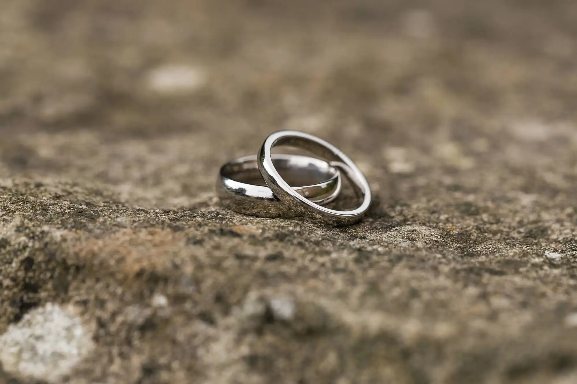 Two silver wedding bands linked together, resting on a textured stone surface.
