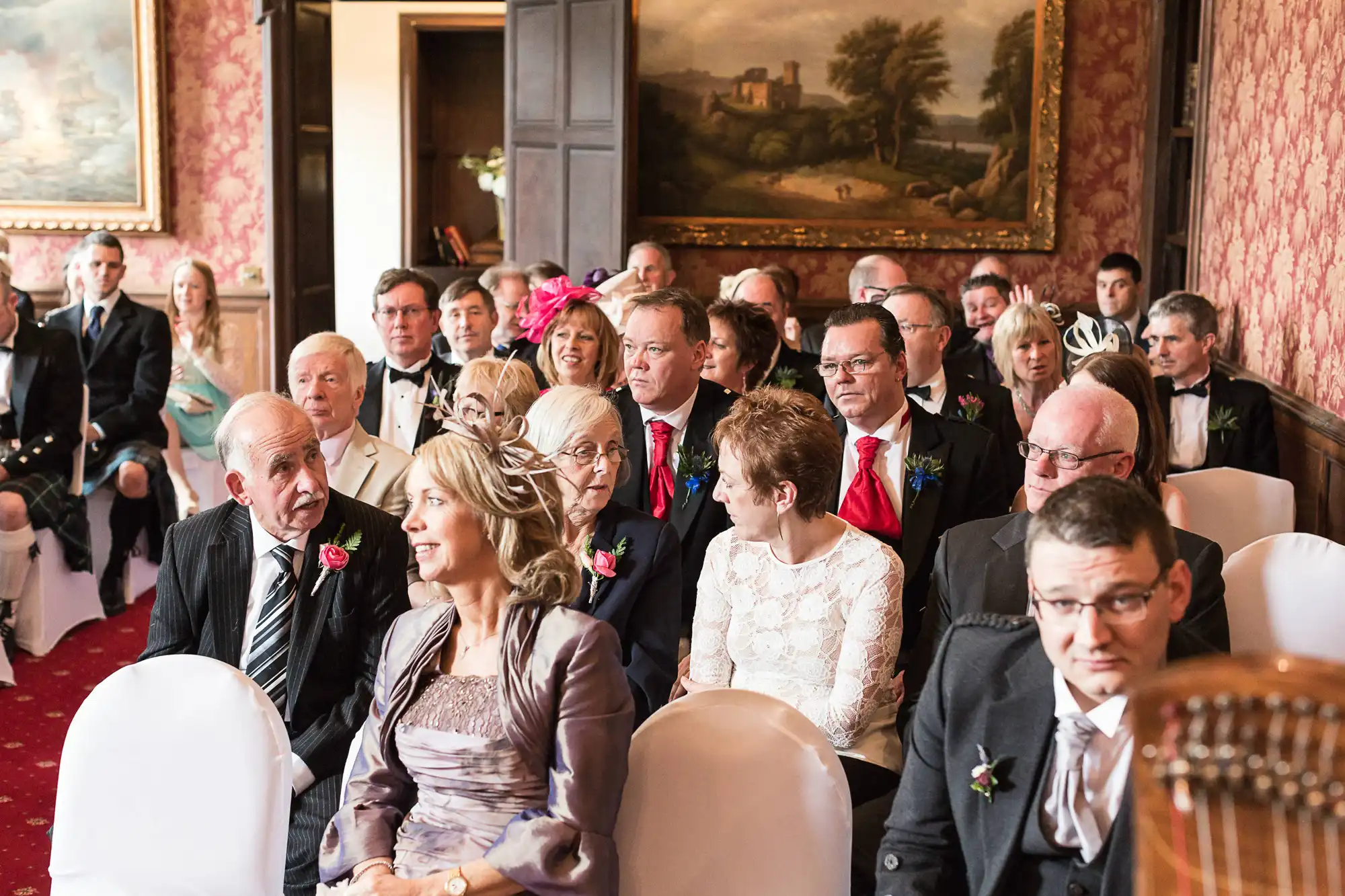 Guests seated at a wedding ceremony in an elegantly decorated room, attentively watching the proceedings.